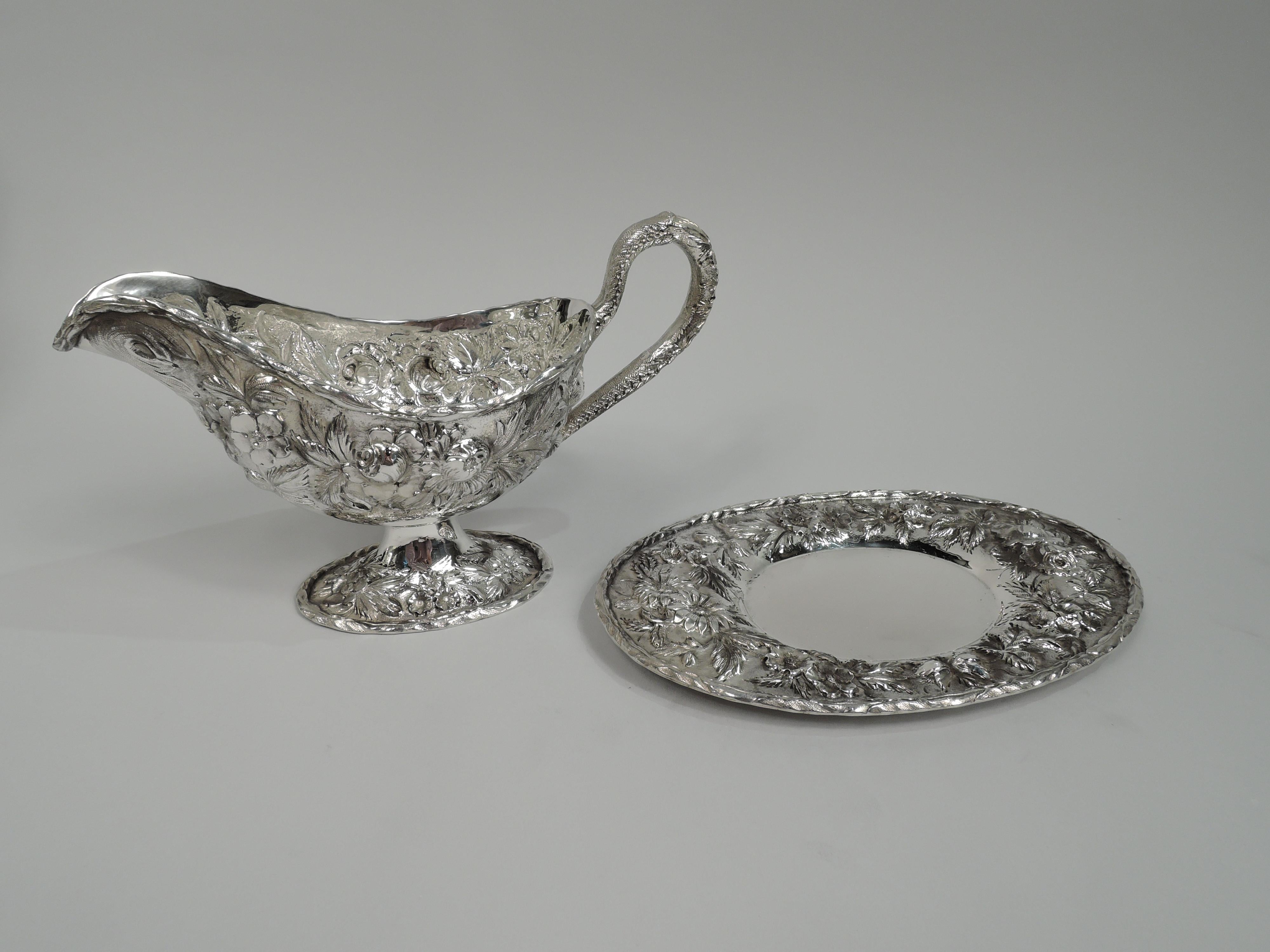 Pretty Edwardian sterling silver gravy boat on stand. Made by S. Kirk & Son Inc. in Baltimore. Boat: Traditional form with high-looping leaf-wrapped handle and raised oval foot. Stand: Plain oval well and wide shoulder. Repousse floral garlands and
