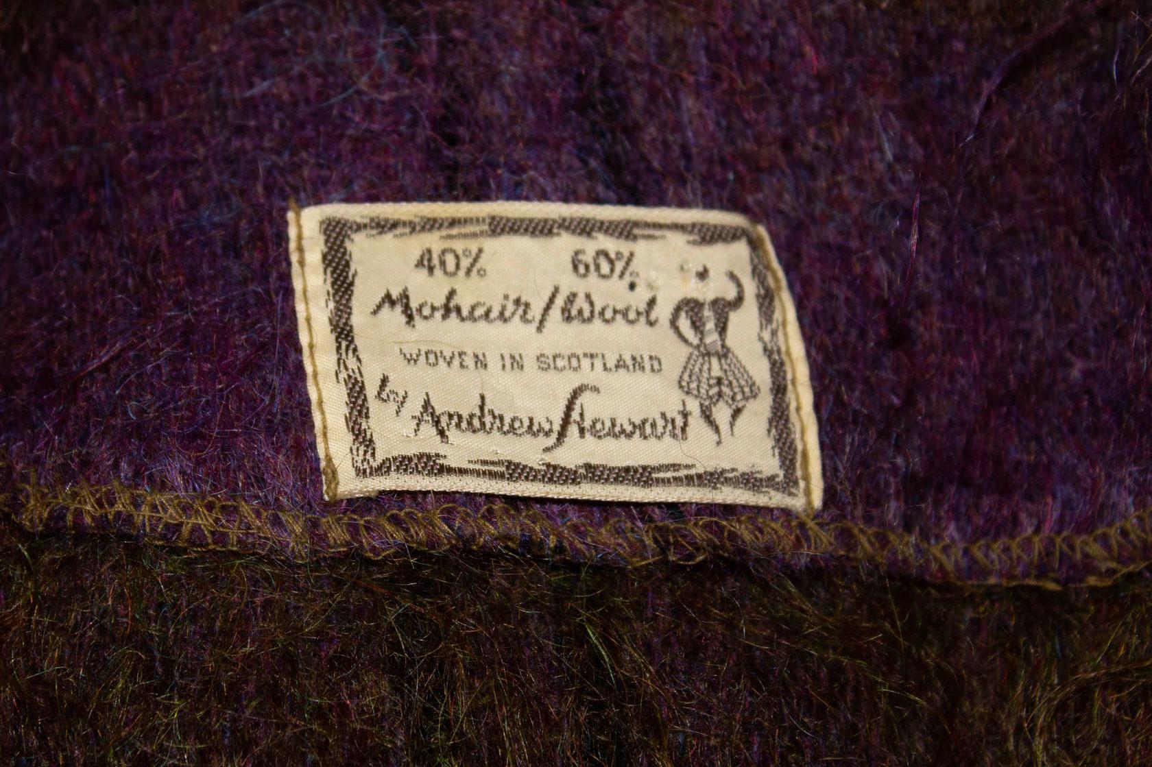 A pretty lilac and green mohair and wool mix cape by  Andrew Stewart of Scotland.  The cape has a popper fastening at the front and fringe detail at the hem. Measurements: Shoulder to shoulder  23'', length 22''