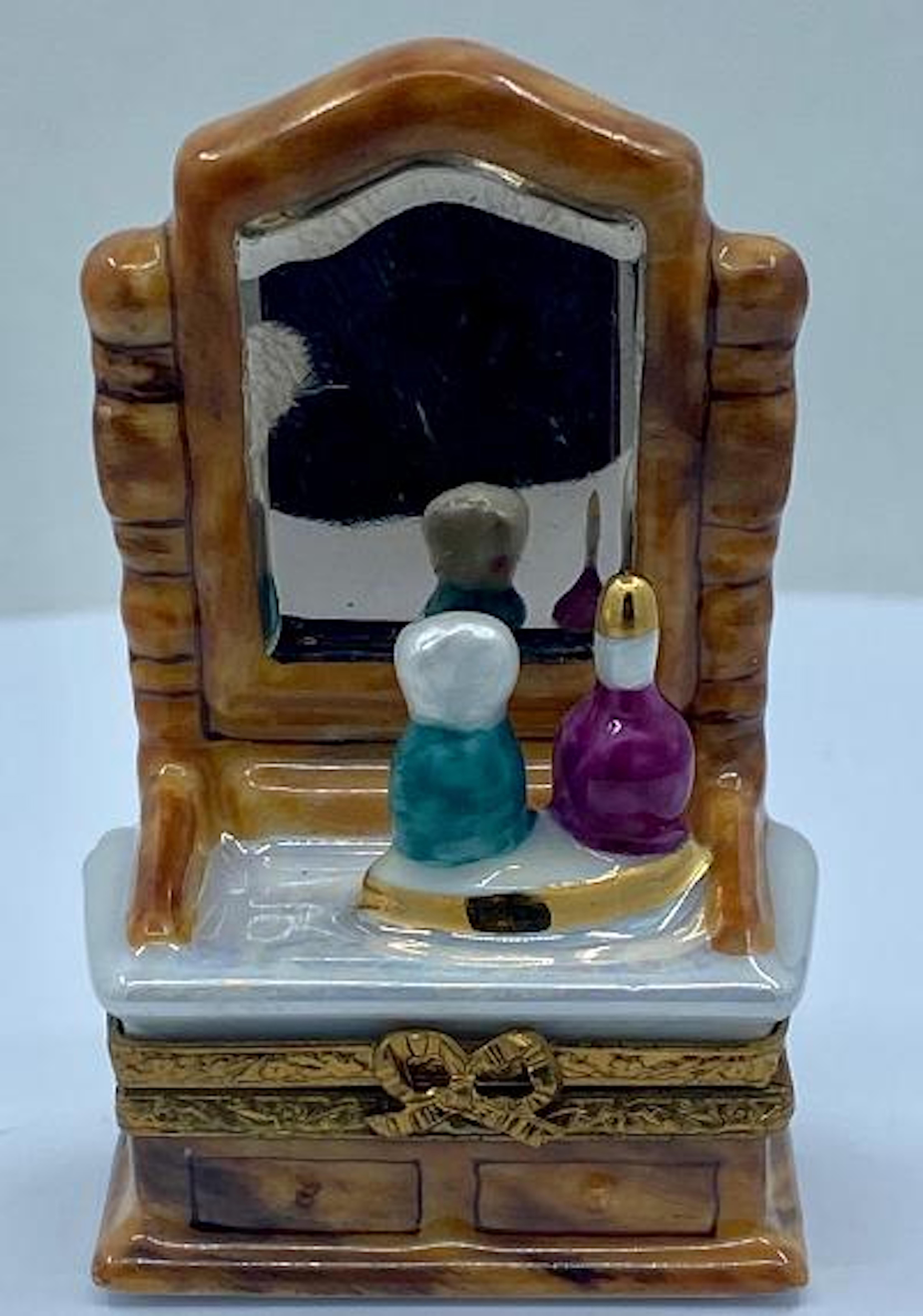Collectible and very unique, Limoges porcelain miniature trinket box is handmade and hand painted in France and features a very detailed vanity or dresser with attached mirror and a tray on top with perfume bottles. Beautiful wood grain finish,