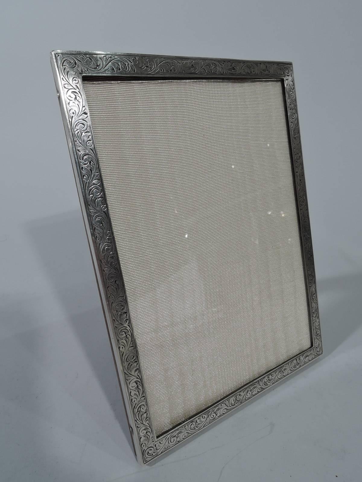 Pretty old-fashioned sterling silver picture frame. Made by Charles S. Green & Co., Ltd in Birmingham in 1953. Rectangular window bordered by engraved scrollwork. With glass, silk lining, and stained-wood back and hinged support for portrait