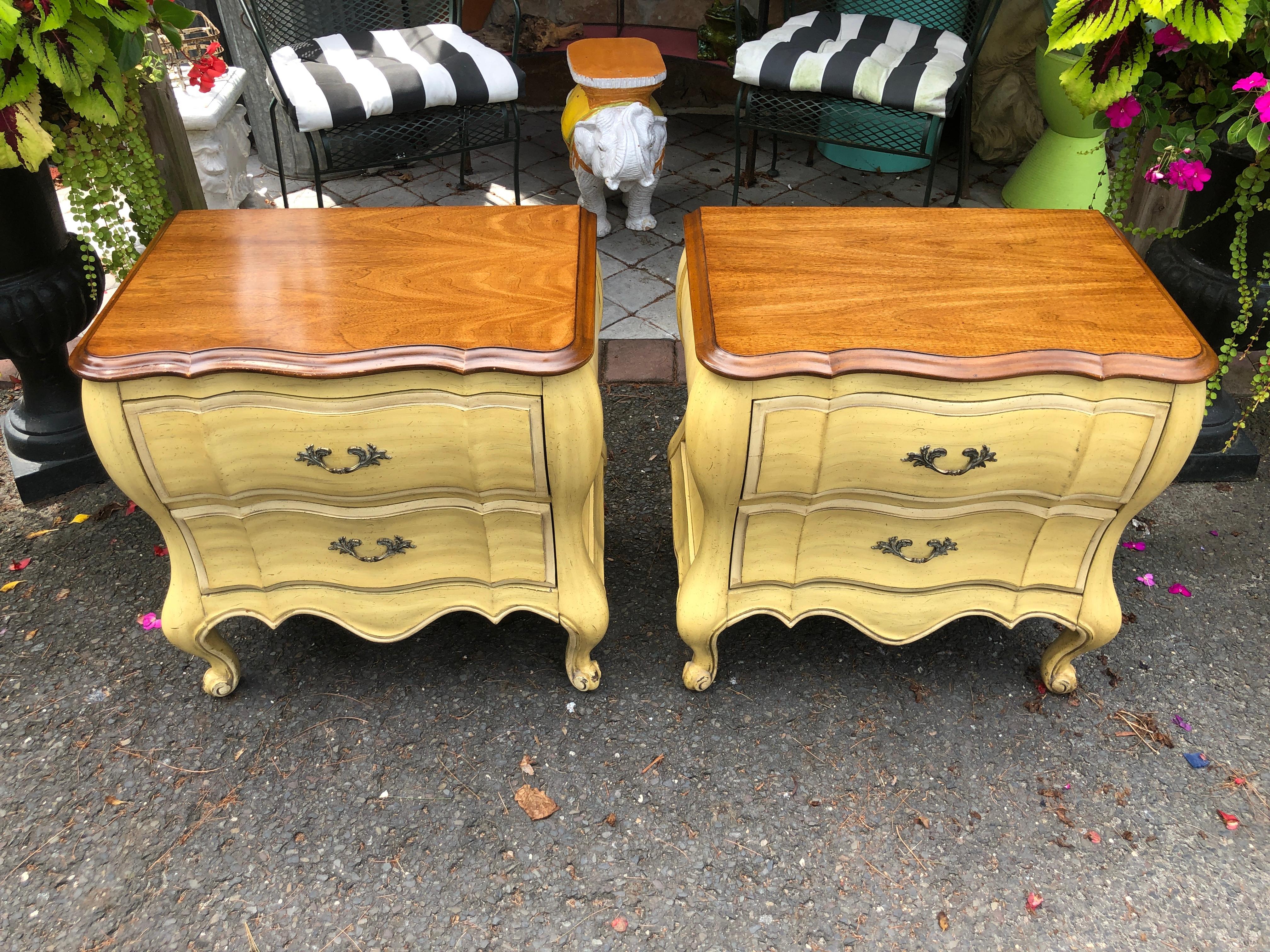 Pretty pair of Dorothy Draper style French Provincial night stands.  We love the yellow glazed distressed finish contrasted with the walnut top. The original owners had custom glasses made for the tops.  These lovely stands measure 25.5