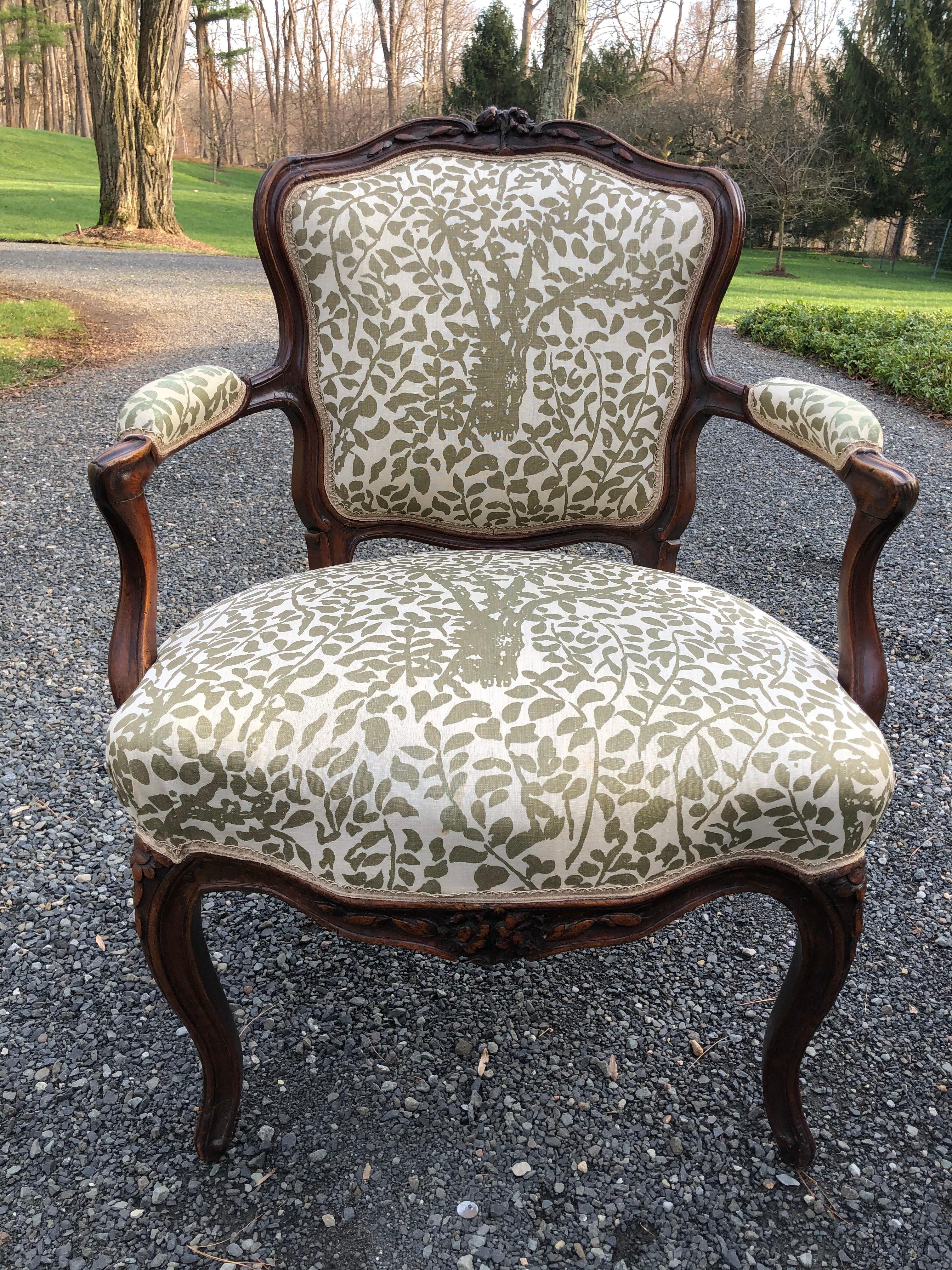 Very pretty pair of French Louis XV carved walnut his and her chairs upholstered in a versatile taupe and off-white fabric with tree and leaf design. The backs are upholstered in a complementary windowpane large check. Measurements for larger chair