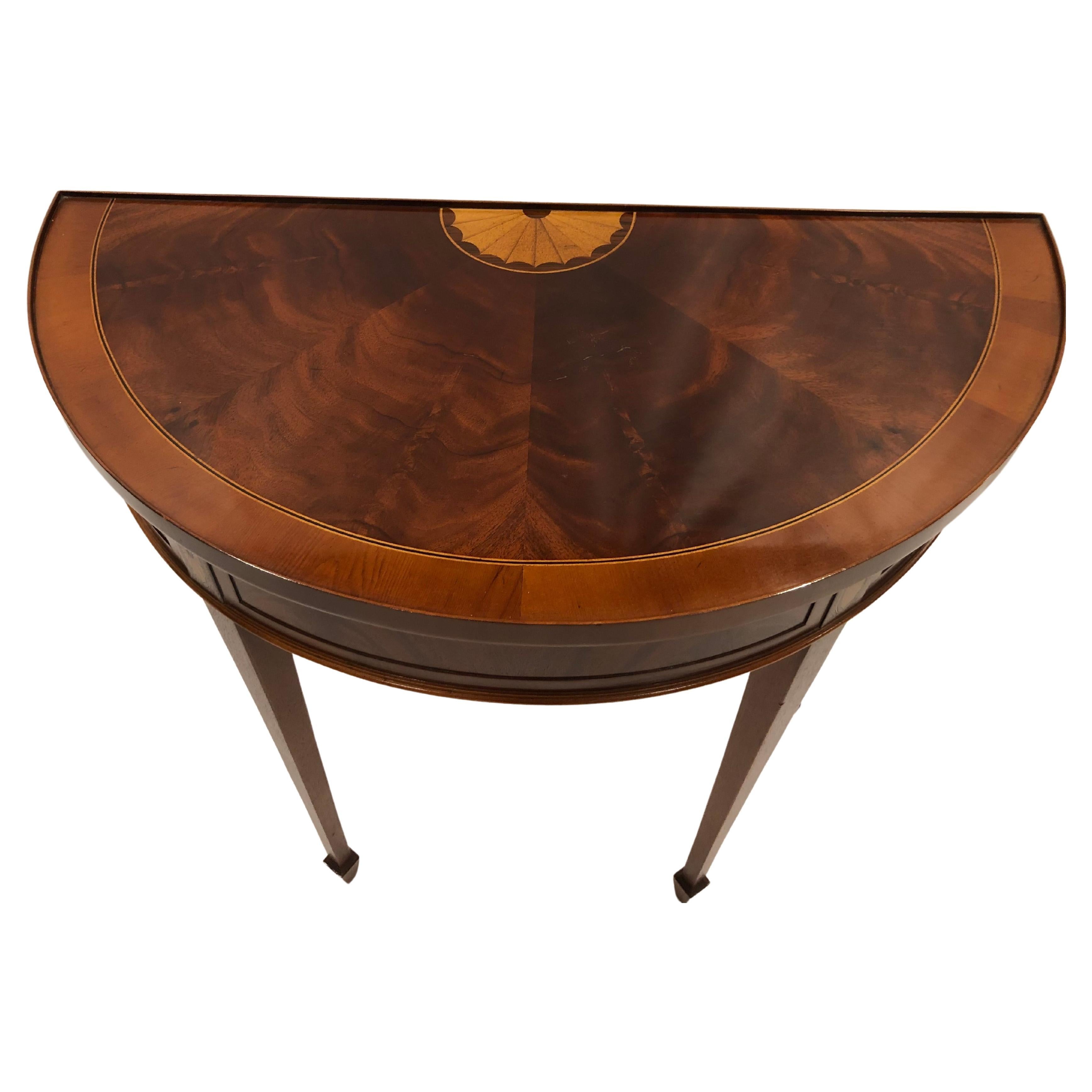 Classic diminutive demilune console having gorgeously grained flame mahogany with fan shaped fruitwood inlay decoration at the back. Tapered elegant legs complete the lovely silhouette.