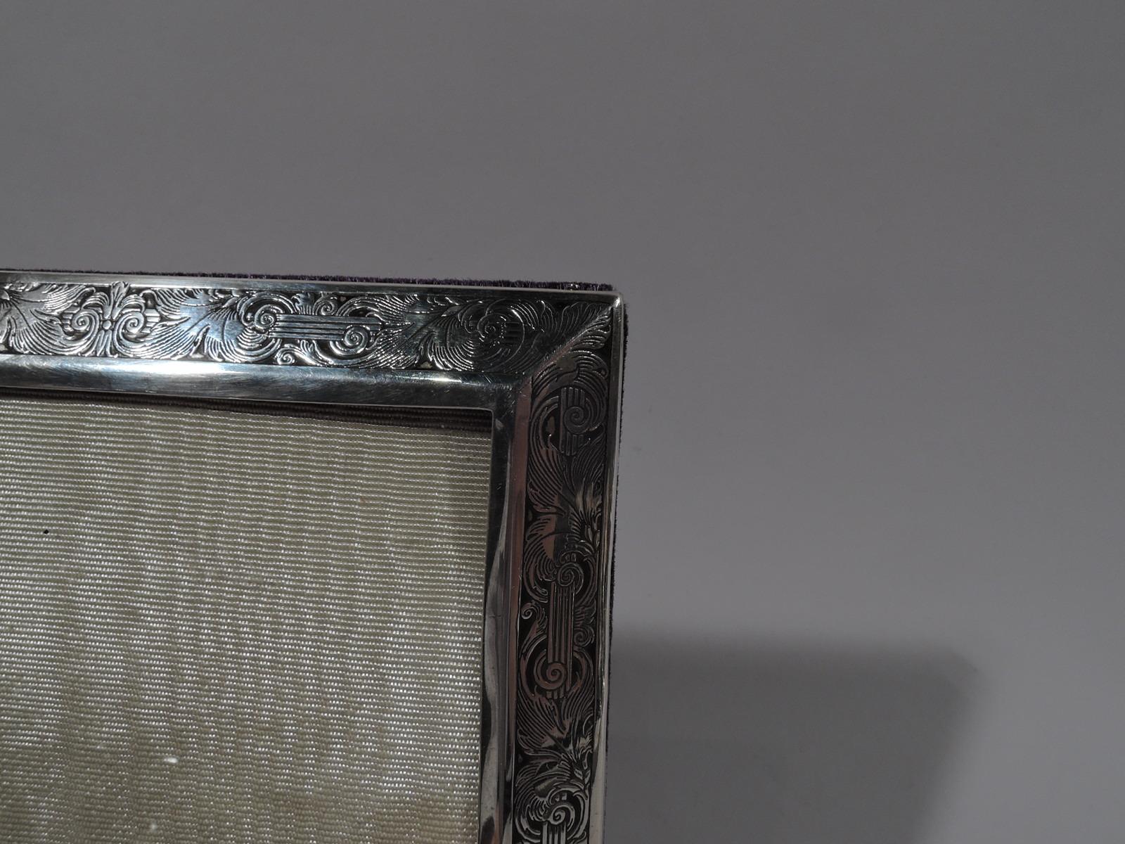 Pretty turn-of-the-century sterling silver picture frame. Made by William B. Kerr in Newark. Rectangular window and canted surround with acid-etched wraparound lines entwined with rinceaux ornament. Shaped cartouche (vacant). With glass, silk