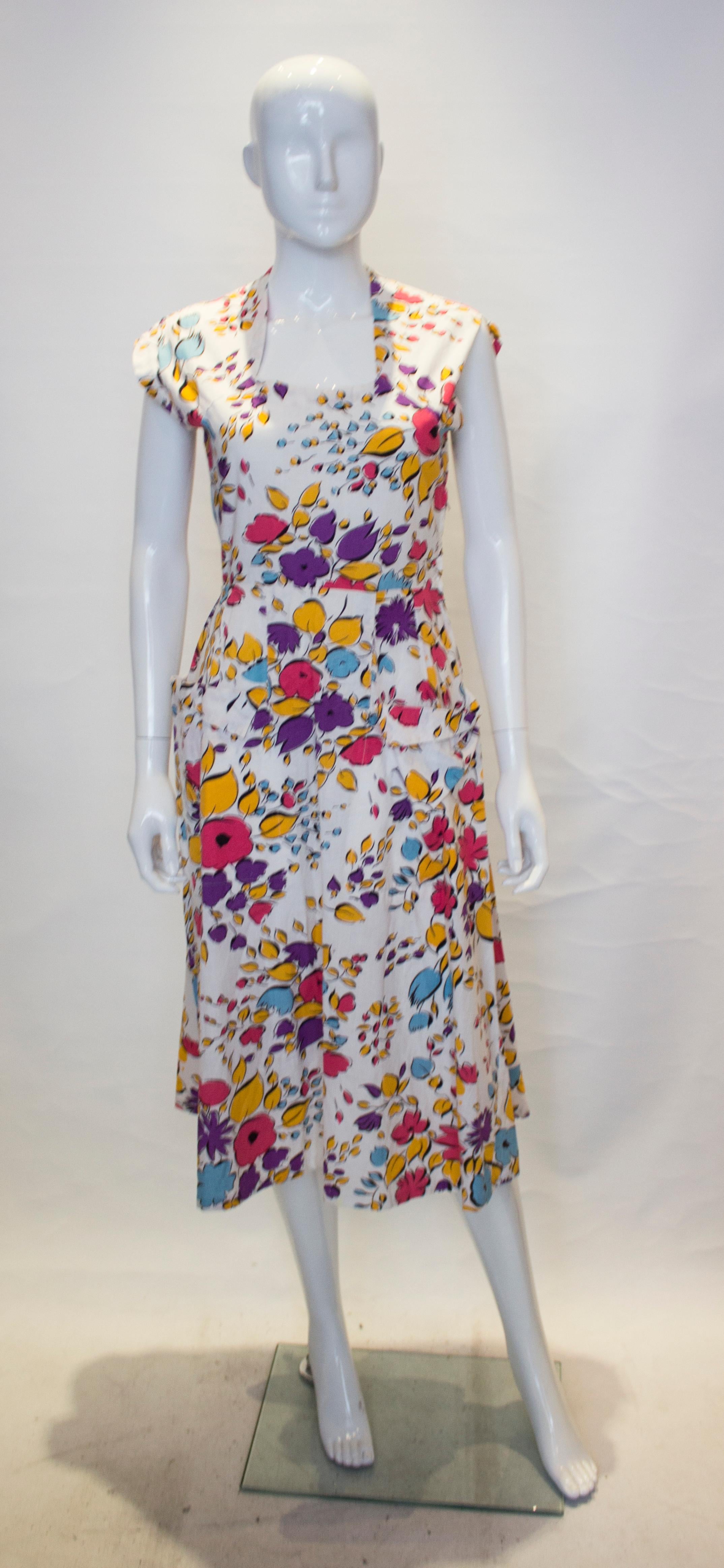 Ein hübsches und leicht zu tragendes Vintage-Sommerkleid. Das Kleid ist aus Baumwolle mit  mit weißem Hintergrund und Blumendruck.  Es hat einen quadratischen Ausschnitt, einen seitlichen Reißverschluss und zwei Taschen auf der Vorderseite.