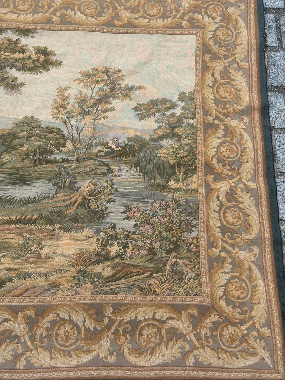 Entdecken Sie die Eleganz dieses exquisiten französischen Wandteppichs, der eine bezaubernde Szene eines Brunnens in der Natur zwischen Bäumen zeigt, die von Flüssen umgeben sind. All dies ist von Rabatten mit fallendem Laub und Palmetten umgeben.