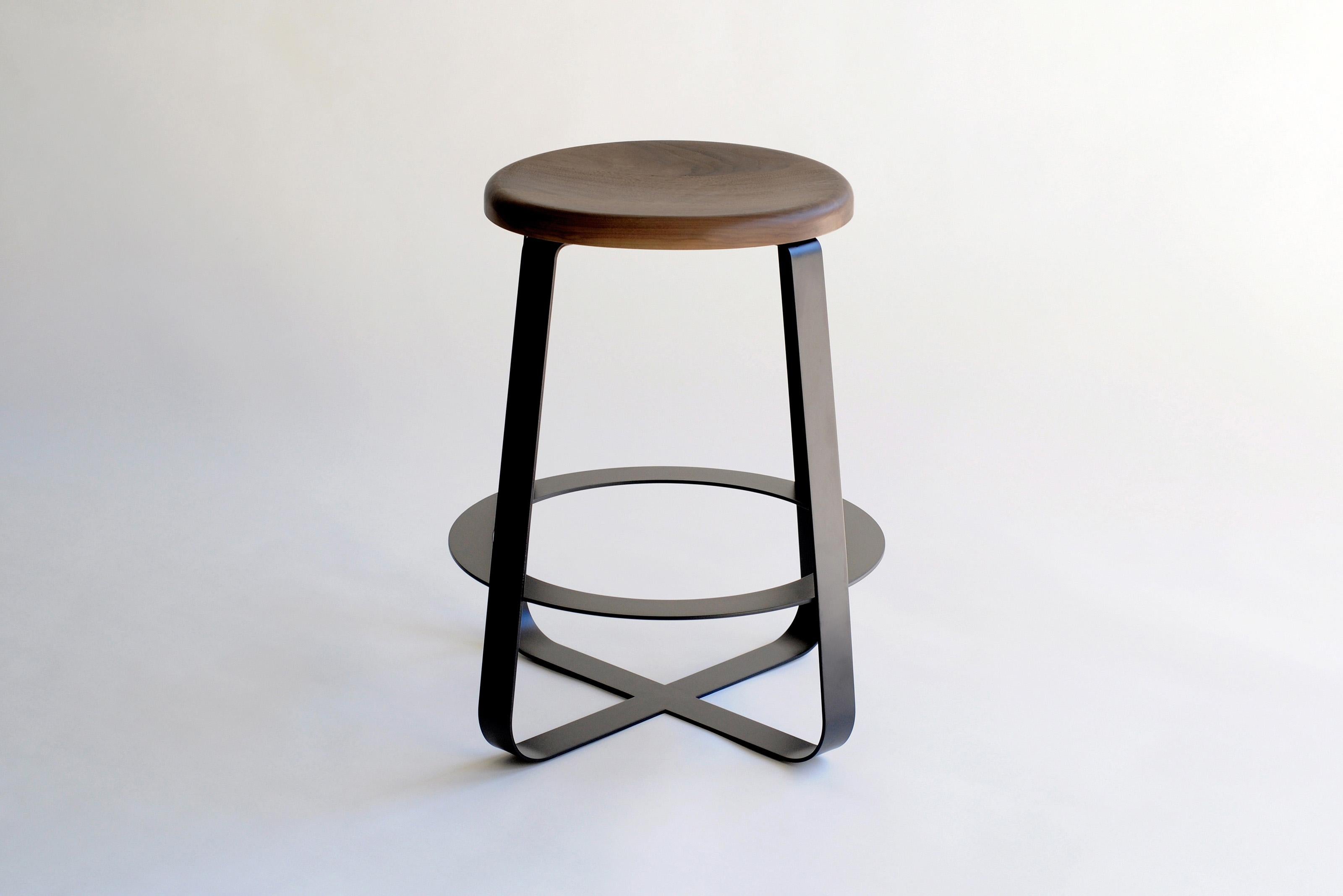 Primi Bar Stool by Phase Design
Dimensions: Ø 54.6 x H 72.4 cm. 
Materials: Powder-coated steel and walnut.

Solid steel flat bar available in a flat black or white powder coat finish with carved walnut, white ash, or upholstered top. Powder coat