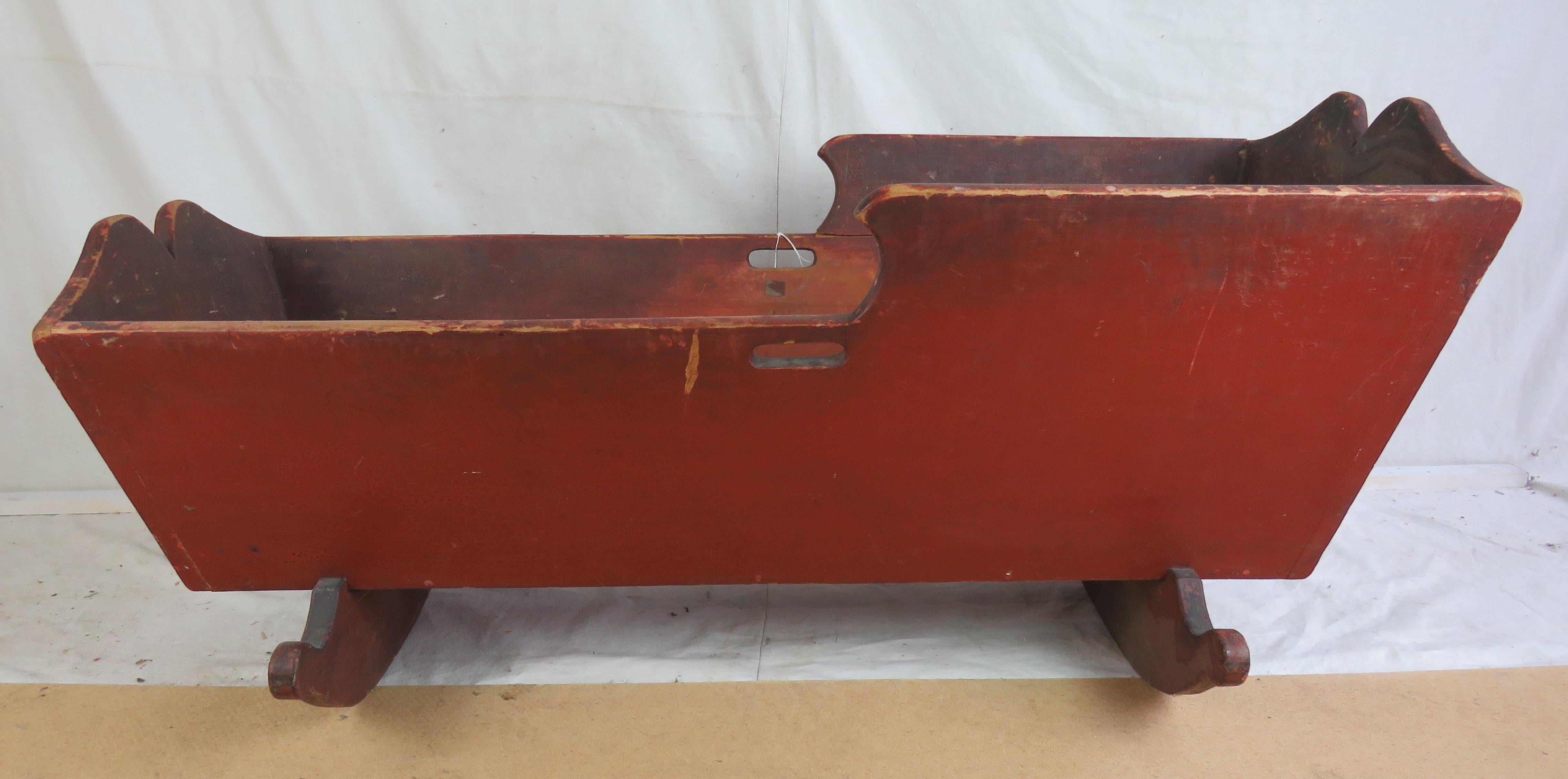 19th Century rocking cradle in original red paint, with shaped detail at head and foot, on carved rockers. Old age crack along one side.