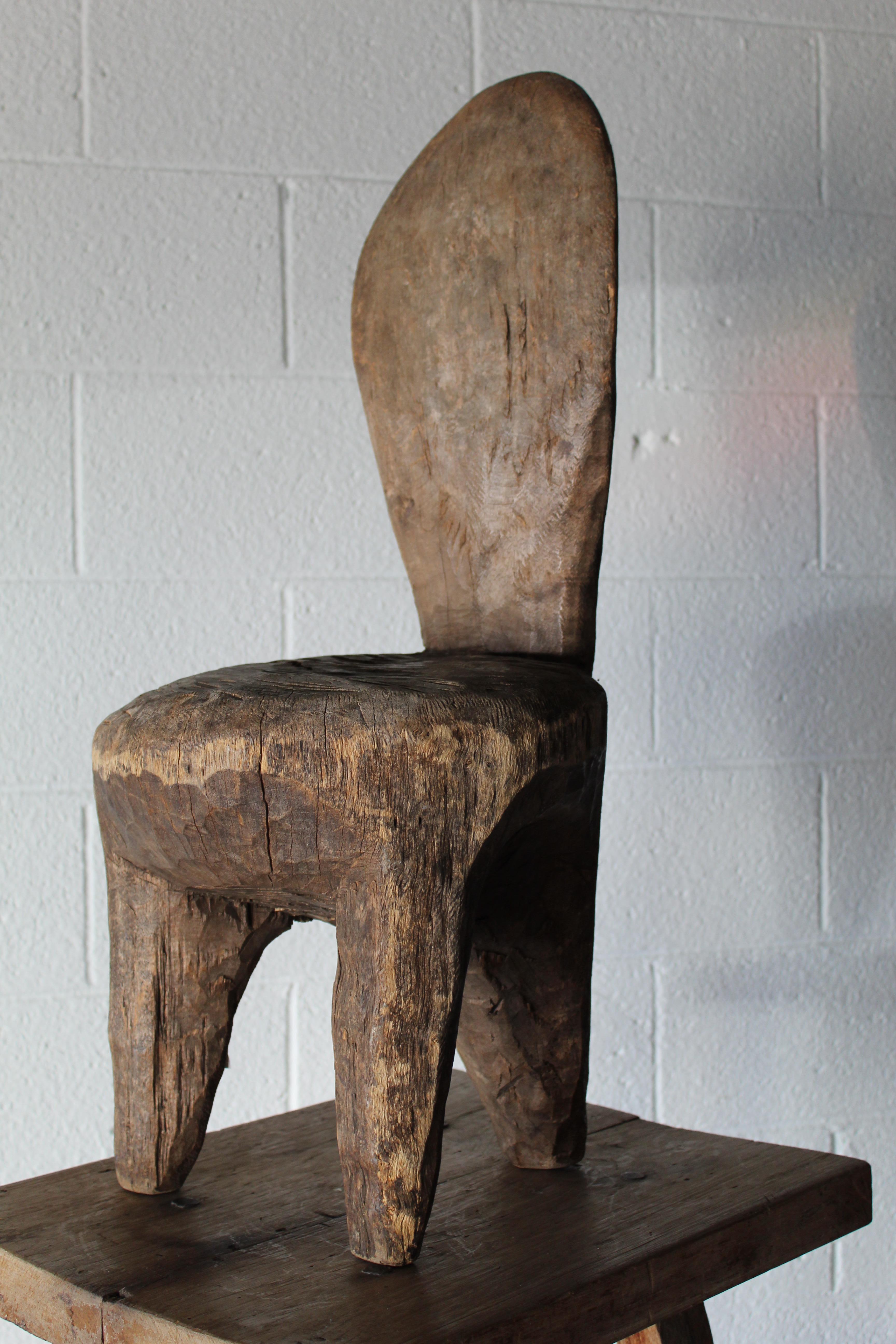 An extremely charming piece, this is a trip leg primitive carved African child's chair. Carved from a single piece of wood, it does have a small and old wood split in the seat, early 20th century.