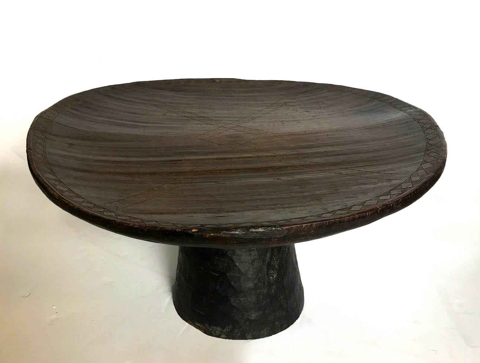 Dark, almost ebony color tribal table carved out of one piece of wood. It has intricate carved details on top. Top is somewhat bowl like in shape and uneven as it was hand carved. Height varies from about 16-18 inches around the edges. Beautiful