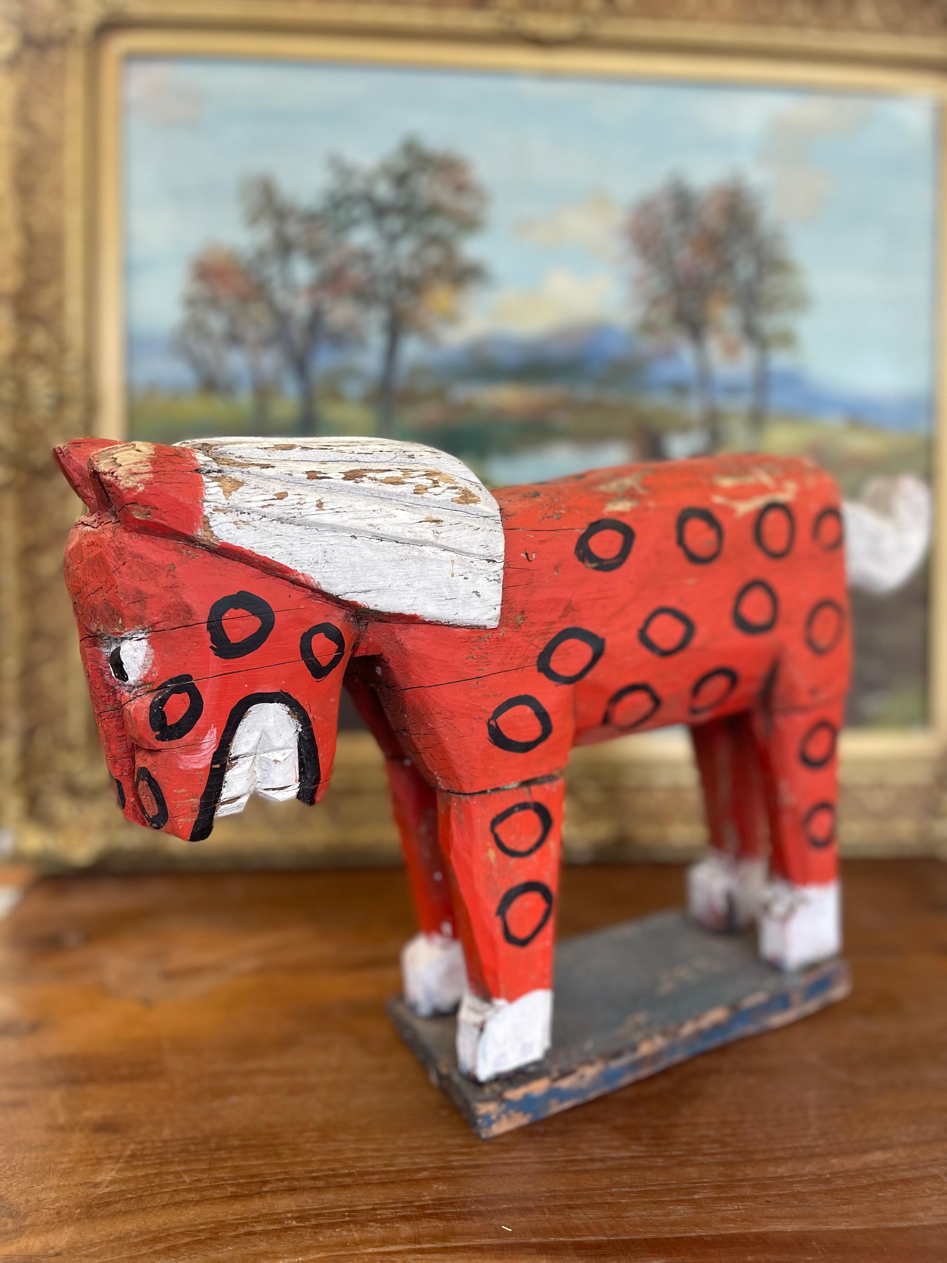  A striking example of early American folk art, the hand carved wooden horse sculpture dates to the early 20th century and showcases the rustic charm and character of outsider craftsmanship. The horse is painted in a bold red with black hand-drawn
