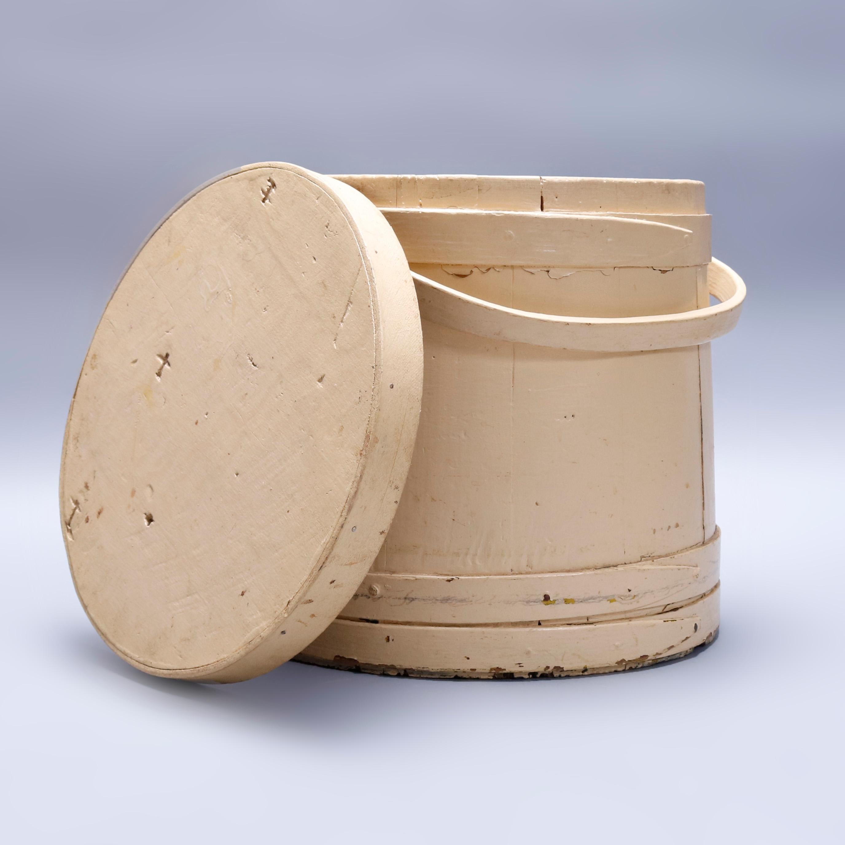 A Primitive Americana Shaker form firkin offers handcrafted four finger wood bucket with painted finish, swivel handle and lid, 19th century

Measures - 19.75