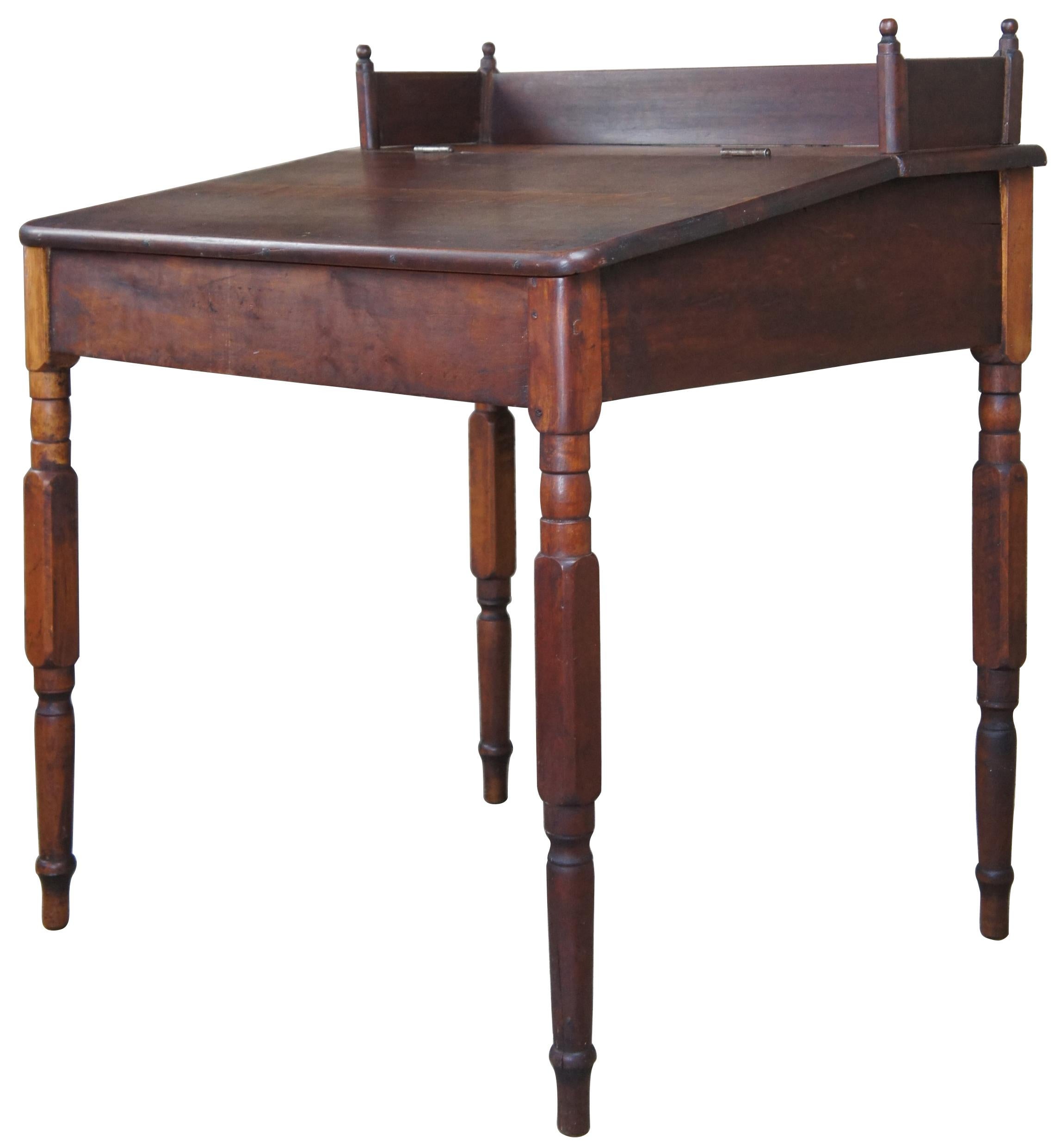A charming 19th century slant top writing desk. Made from cherry with turned legs leading to peg feet. Features a backsplash with turned finials and large storage area underneath top. Measures: 37”.
 