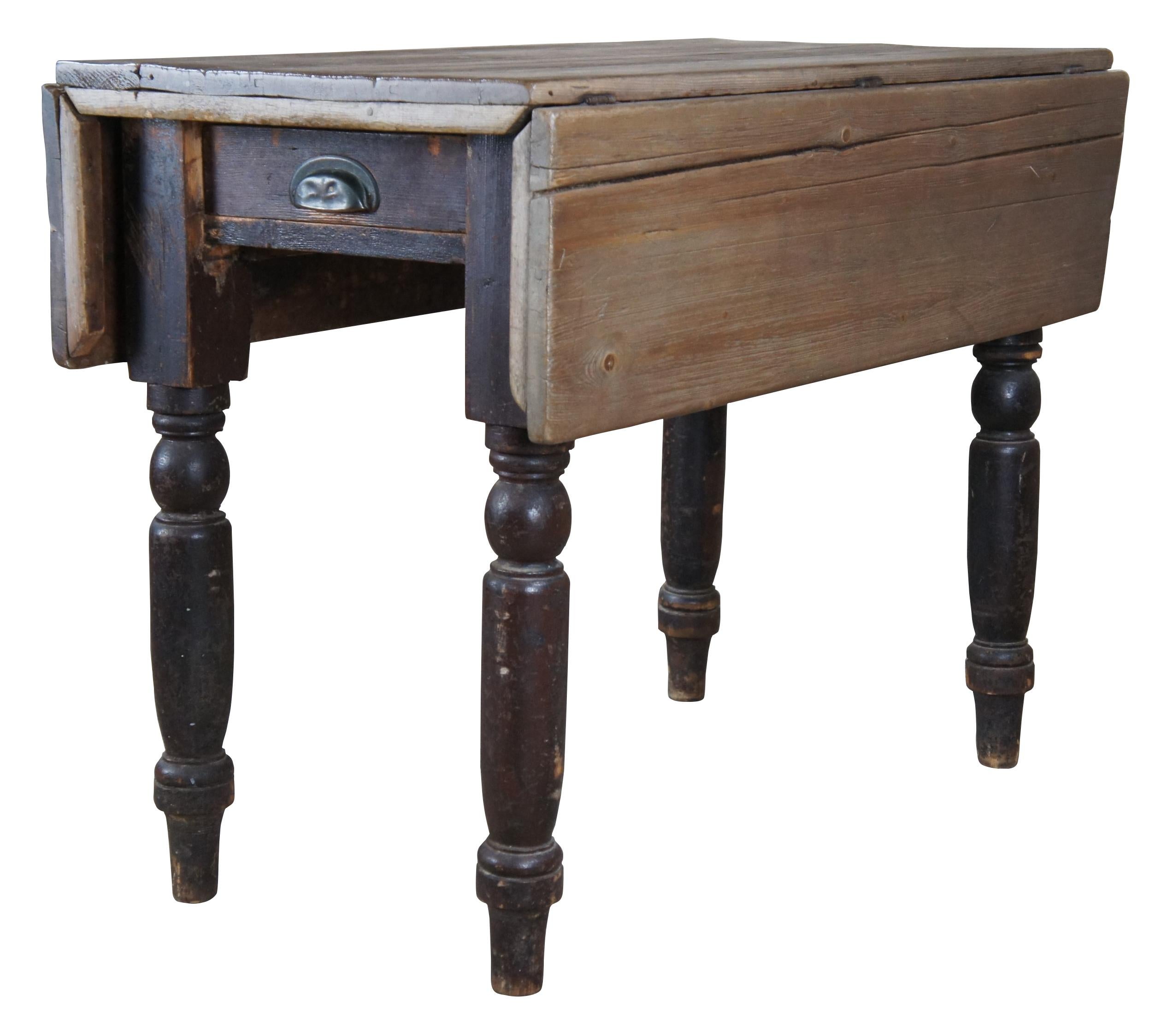 A quaint primitive 19th century English pine farmhouse tavern dropleaf breakfast table or console featuring a rectangular form, central drawer and turned legs. Leafs are supported by iron fold outs. 

37.5
