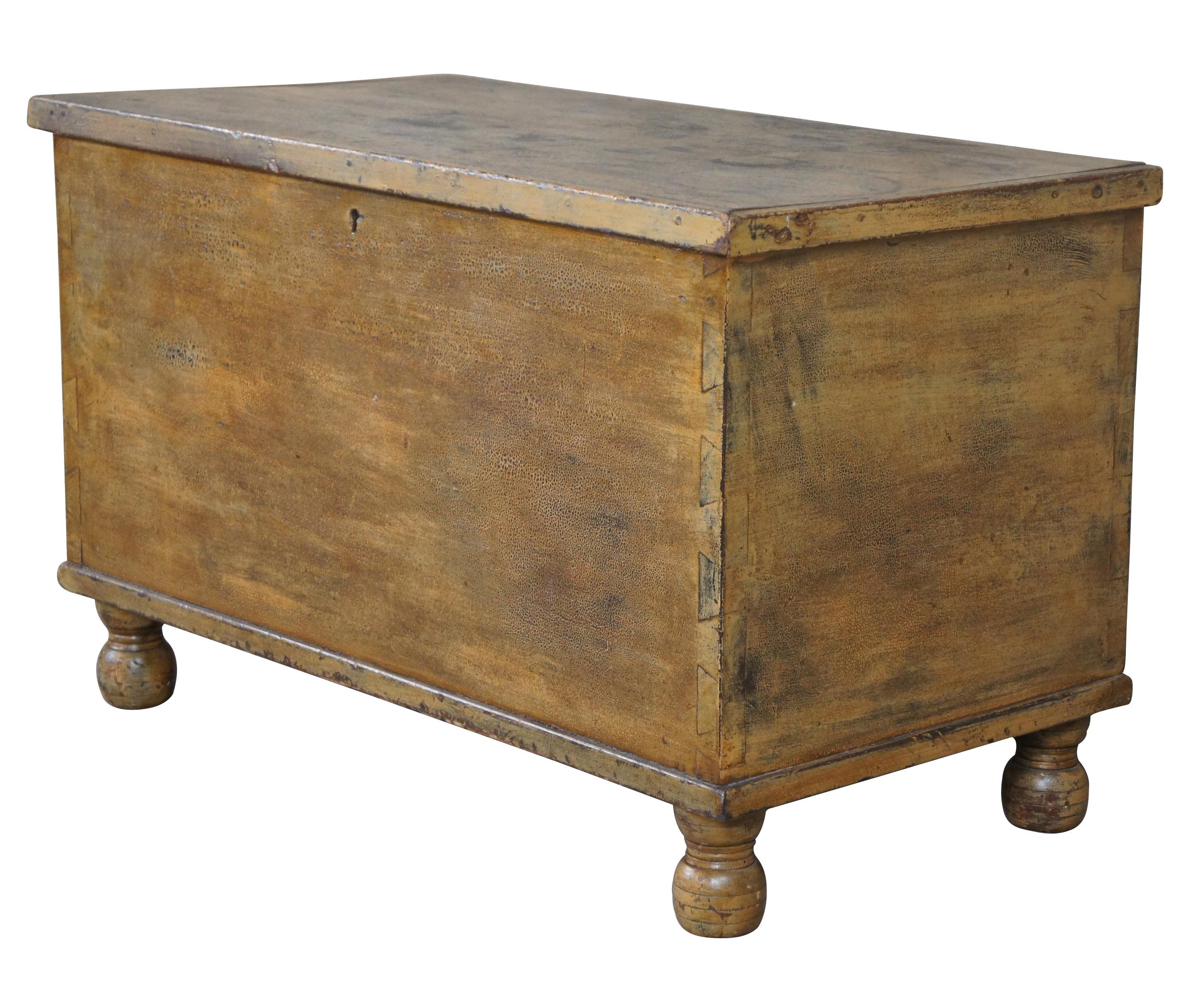 An antique Early American blanket storage chest, Pennsylvania circa 1820-40s. A rectangular form made from pine with a yellowish painted finish. Features a hand dovetailed case, interior compartment (ditty box) and hand turned bun feet. A charming