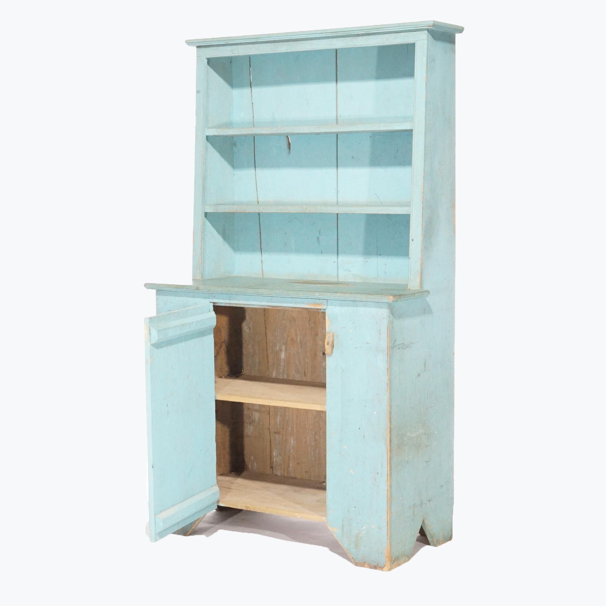 A primitive style step back cupboard offers soft wood construction with distressed blue paint finish, having upper with open shelves over lower single drawer cabinet opening to shelved interior, raised on cut-out legs, 20th century

Measures-