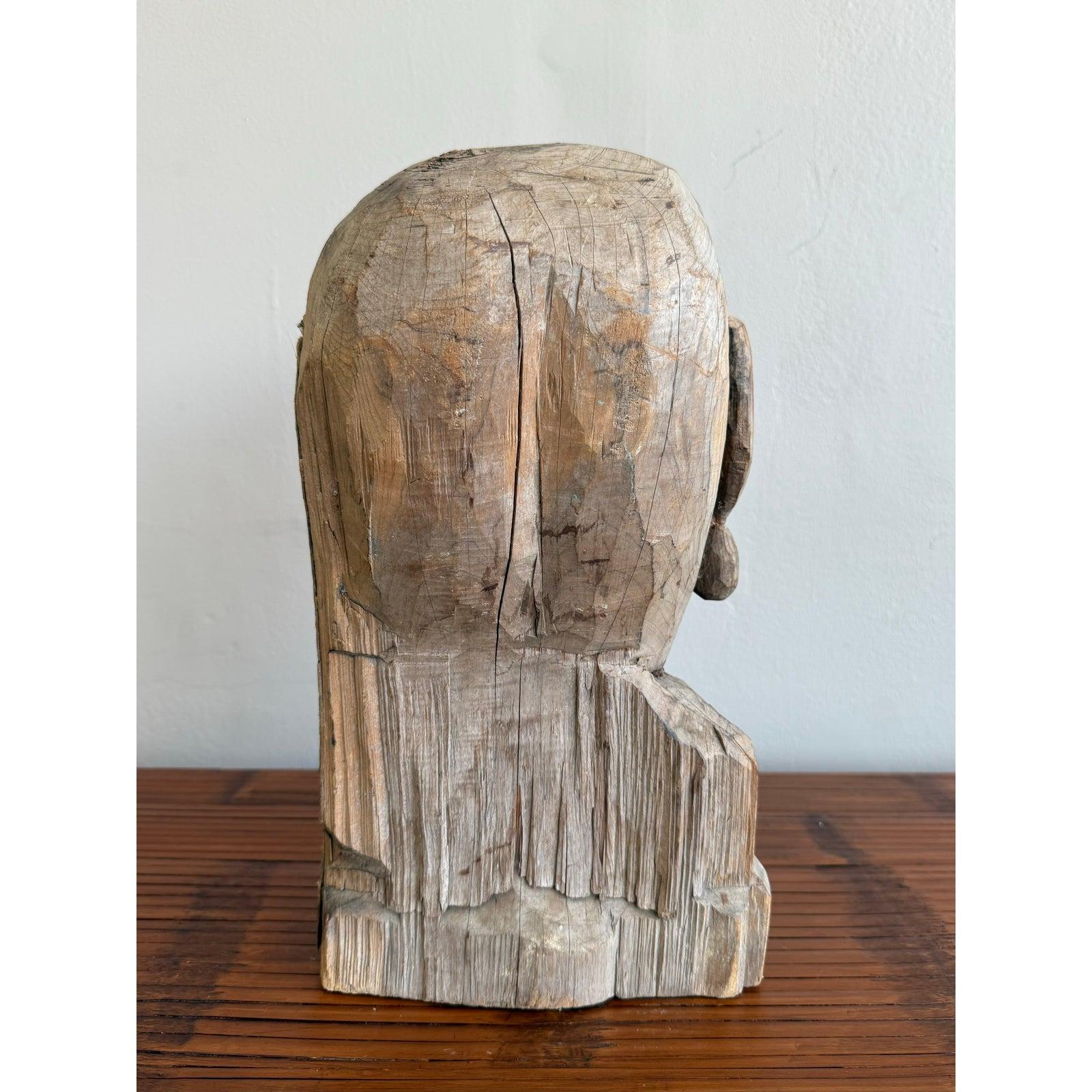 Este busto crudo y expresivo es un poderoso ejemplo de escultura de inspiración outsider o folclórica. Tallada a mano en una sola pieza de madera desgastada, la figura presenta unos rasgos faciales exagerados -sobre todo una nariz larga y prominente