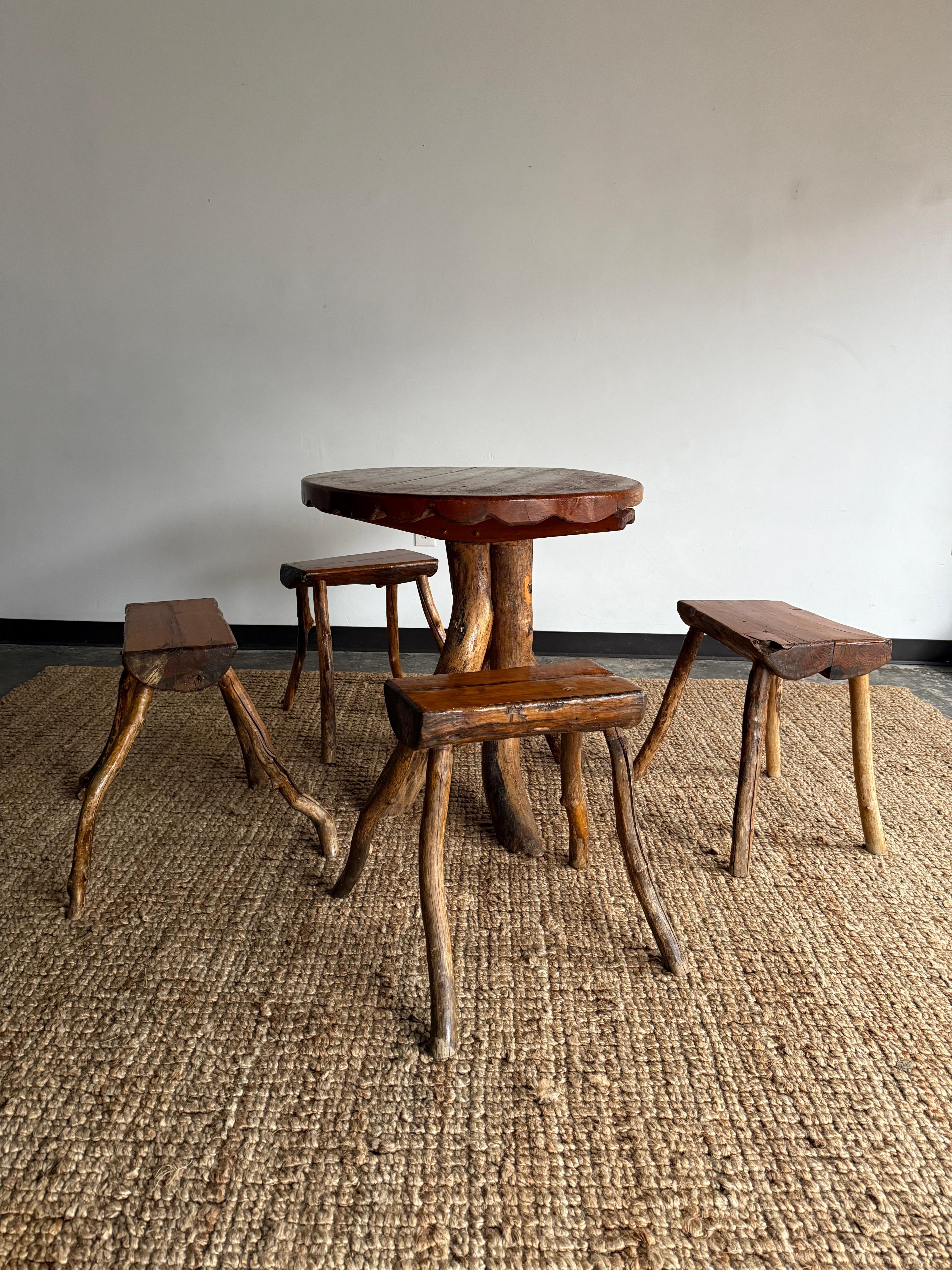  wooden folk/timber-to-table dining table with scalloped edge and log base with four log stools with twig legs. Would pair incredibly with more modern esthetics that may include various stone and leather finishes. In good vintage condition with