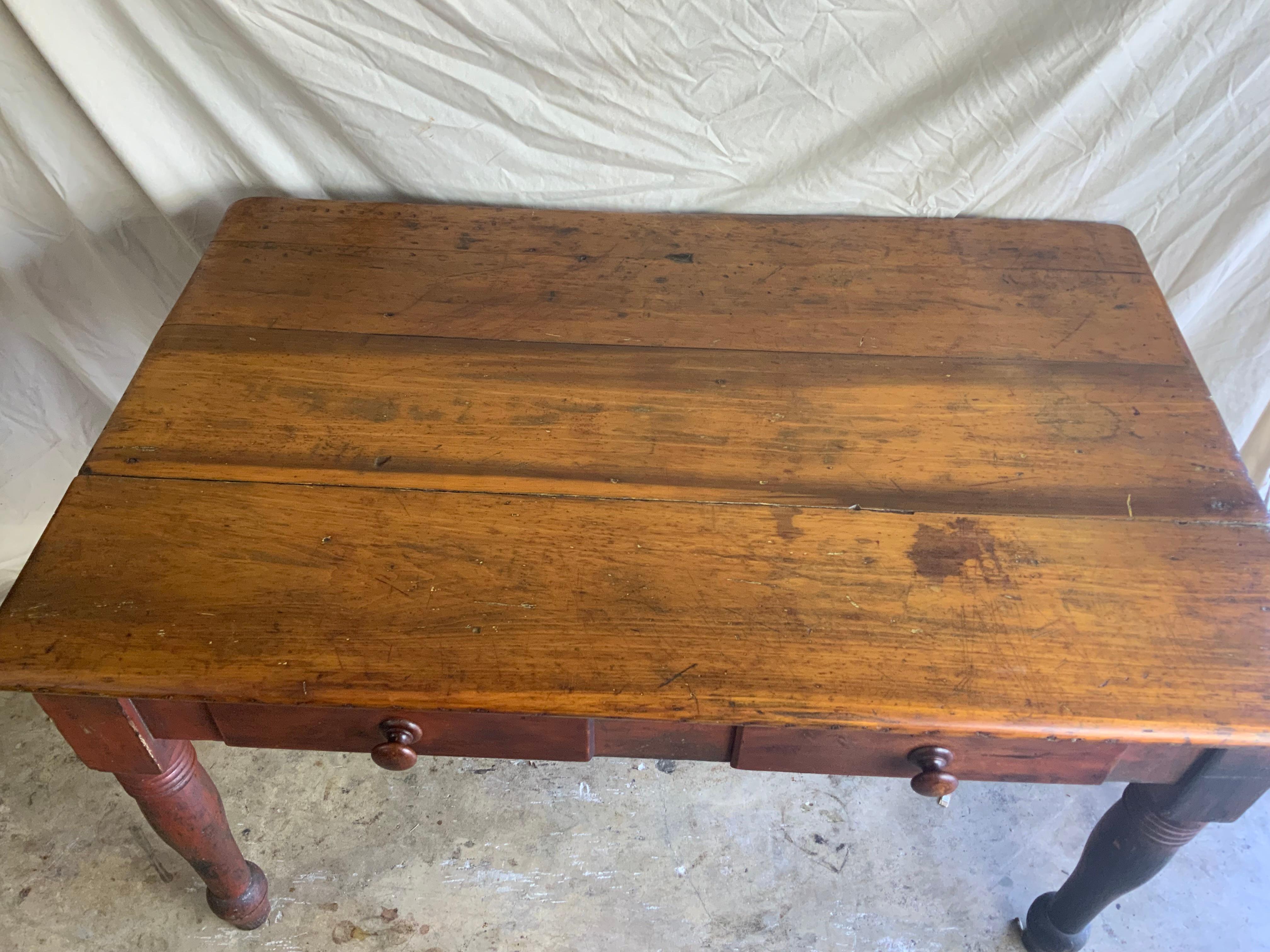 Late 19th / early 20th century primitive Pine Farm table in old red paint. A nice strong heavy table with two drawers, heavy turned legs and a nice wide apron.  Measurement from the floor to the bottom of the apron is 23”.