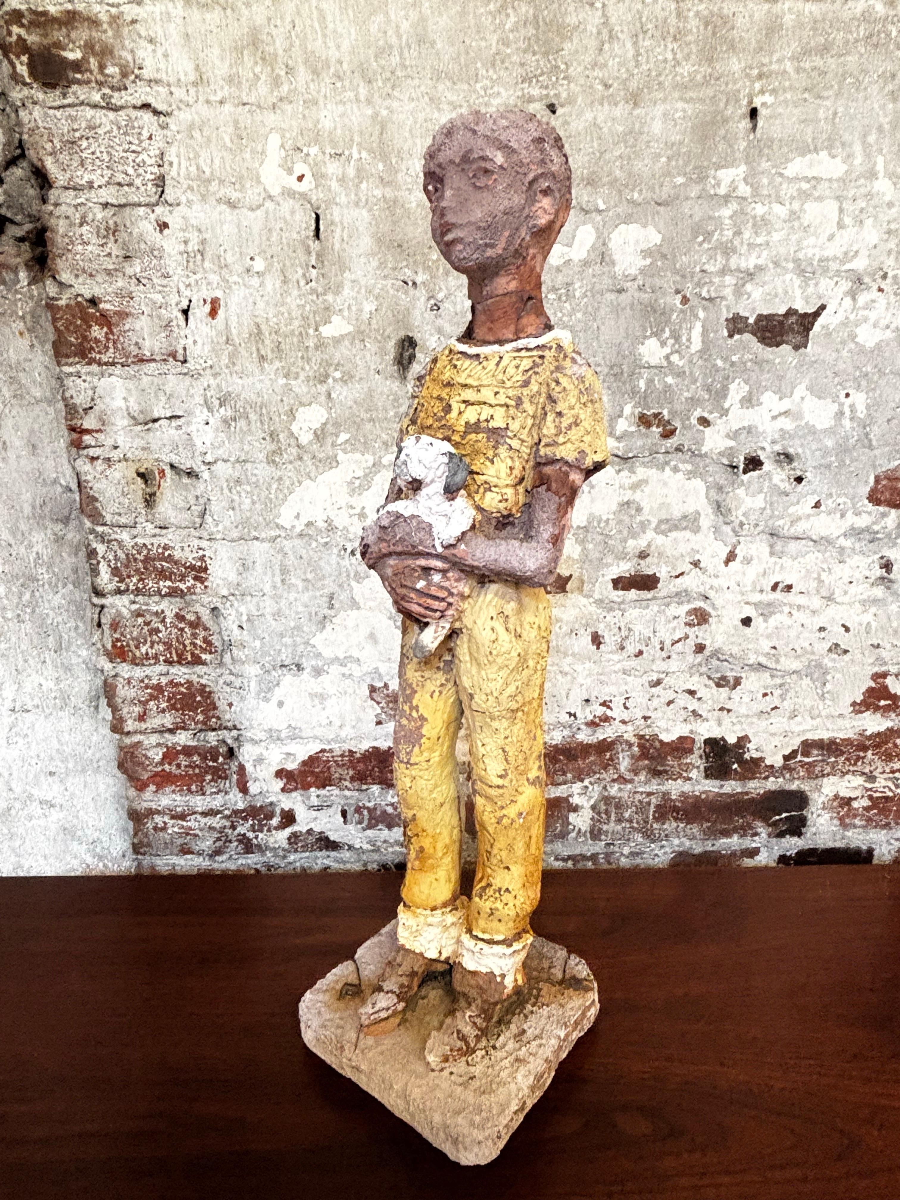 Figura di un ragazzo che tiene in braccio un cane.  La figura sembra essere rimasta all'aperto per molto tempo e gli elementi hanno consumato parte della vernice e del cemento.  Ha un aspetto e una sensazione fantastici!  È stato costruito con
