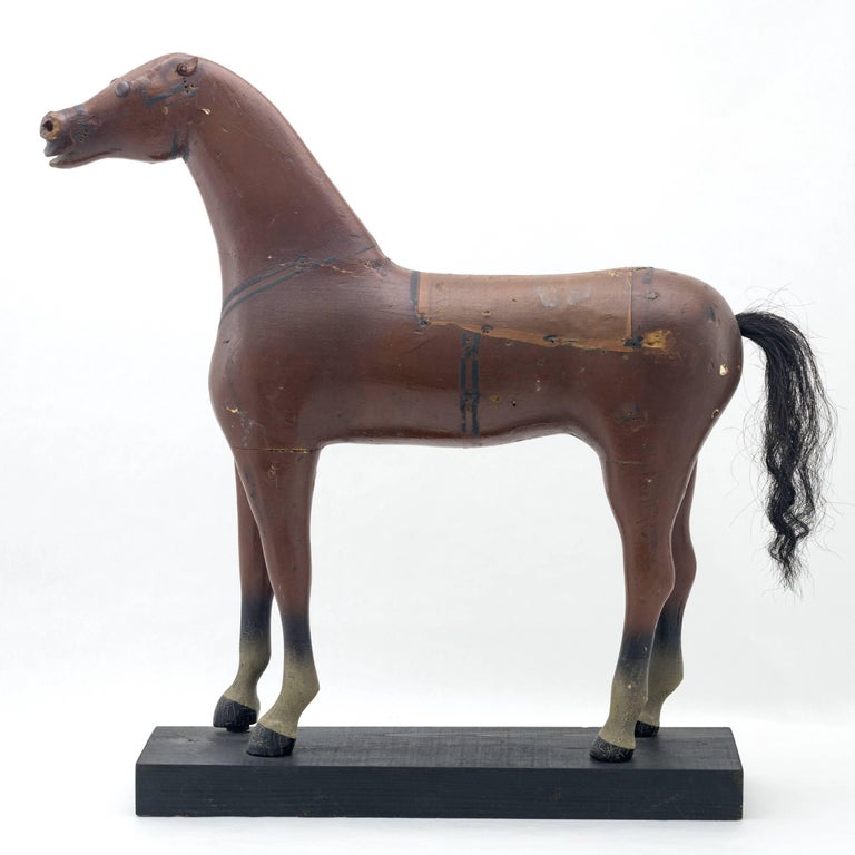 A Folk Art carved wood and gesso painted standing horse
with painted cloth saddle and horse hair tail
Mounted on a later made black painted platform.
 
      
      