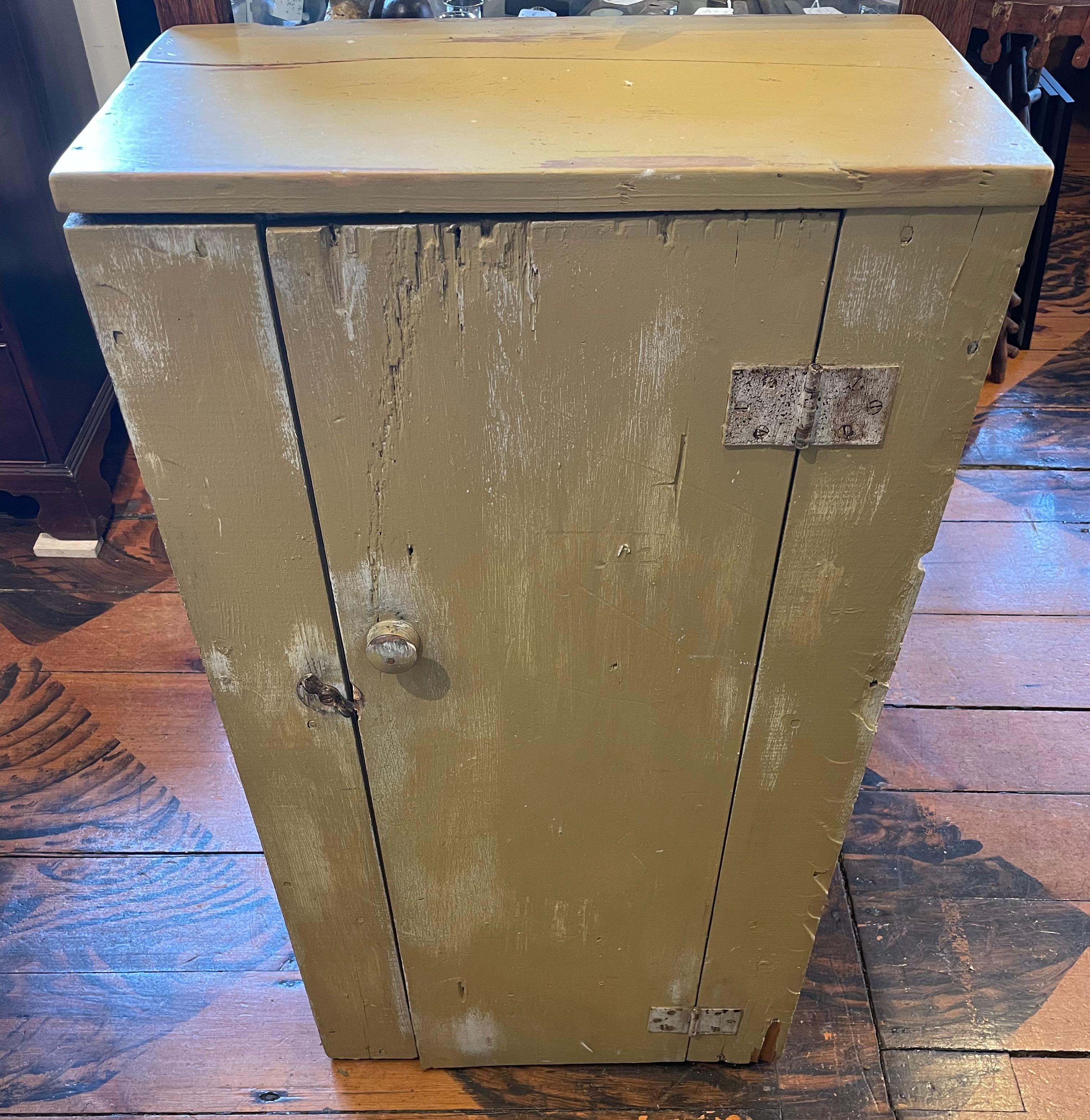 Diminutive rustic jelly jar cupboard, likely homemade, crafted from reclaimed wood. Exterior with mustard yellow/ochre paint, white painted interior with two shelves, iron hinged door 11.75” wide.