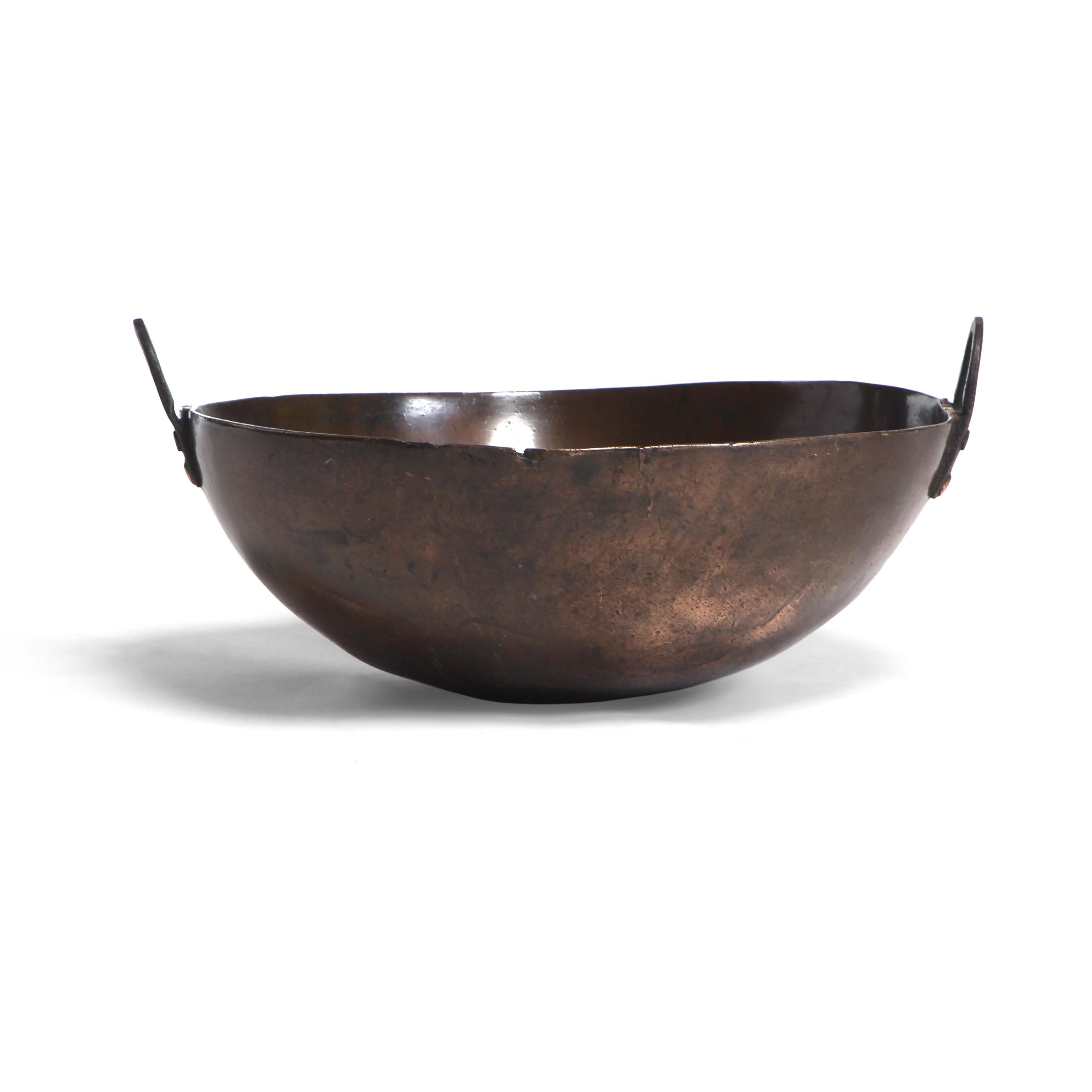 An antique bronze bowl with a rich patina and riveted iron handles.