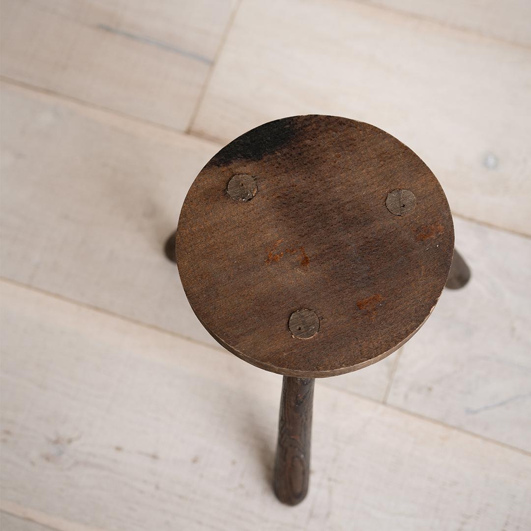 This primitive tripod milking stool, with its rustic patina and hand-hewn silhouette, is a testament to early craftsmanship and utilitarian charm