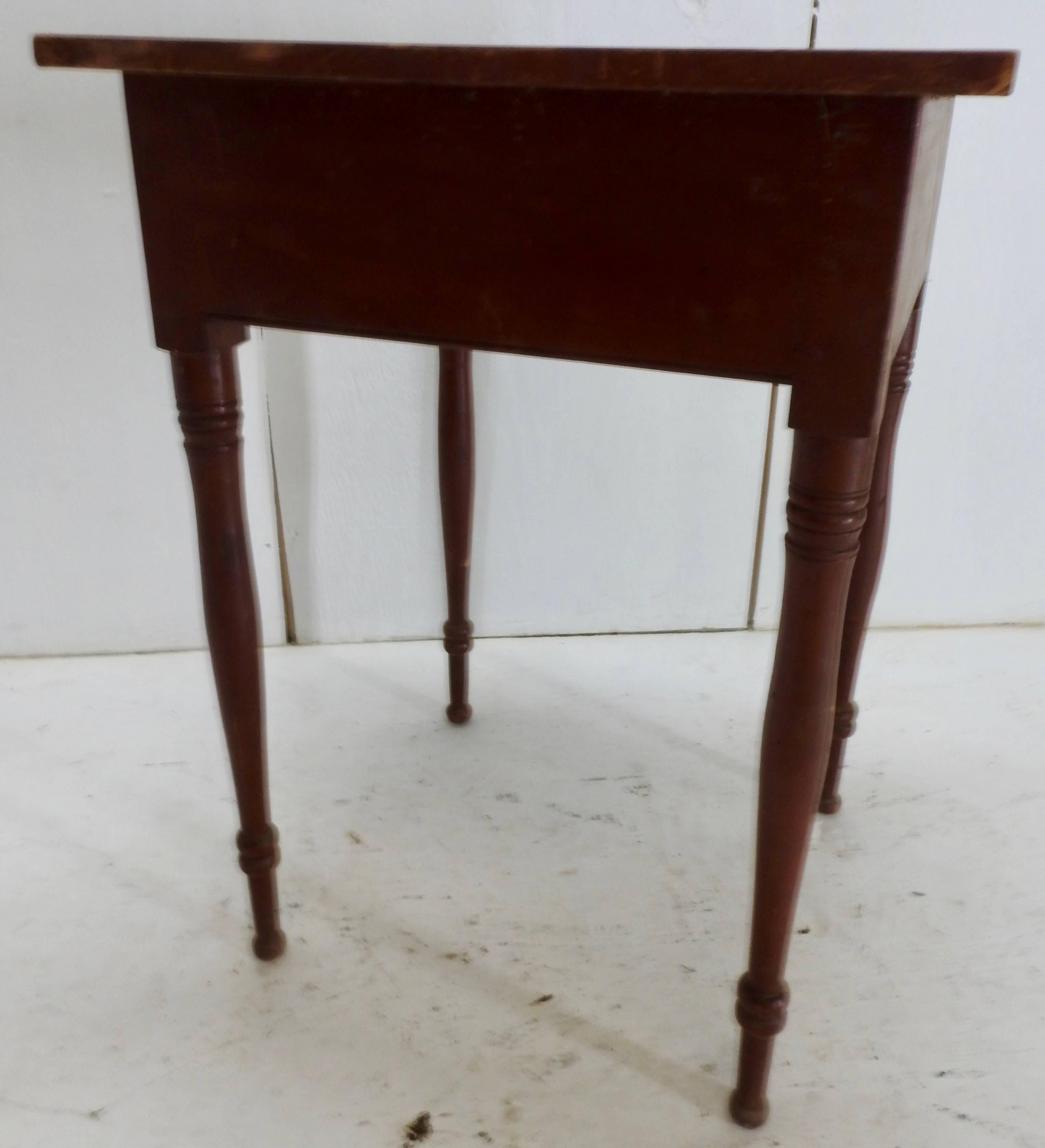 Offering this simple yet beautiful primitive working table featuring a single drawer with dove tailing. It is painted a deep red shade. The four turned spindle legs give the simple lines interest. The top edges have some wear from use. Add this