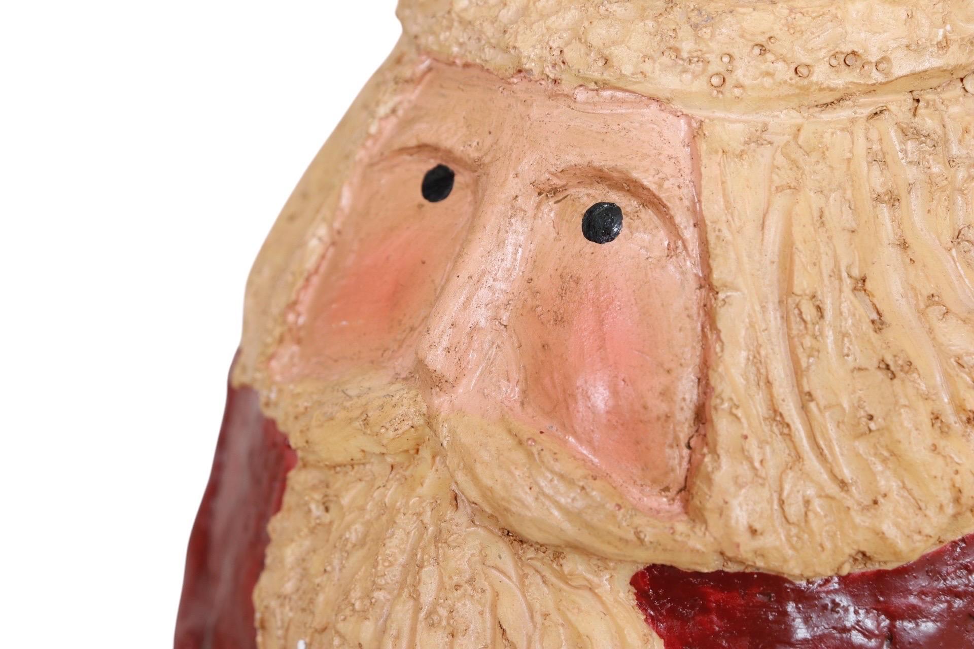 A charming Santa Claus Christmas figure made of chalkware. The primitive style ornament is rounded with primitive features including simple eyes, nose, mustache, and beard, along with the traditional fur trimmed red Santa suit and black gloves.
