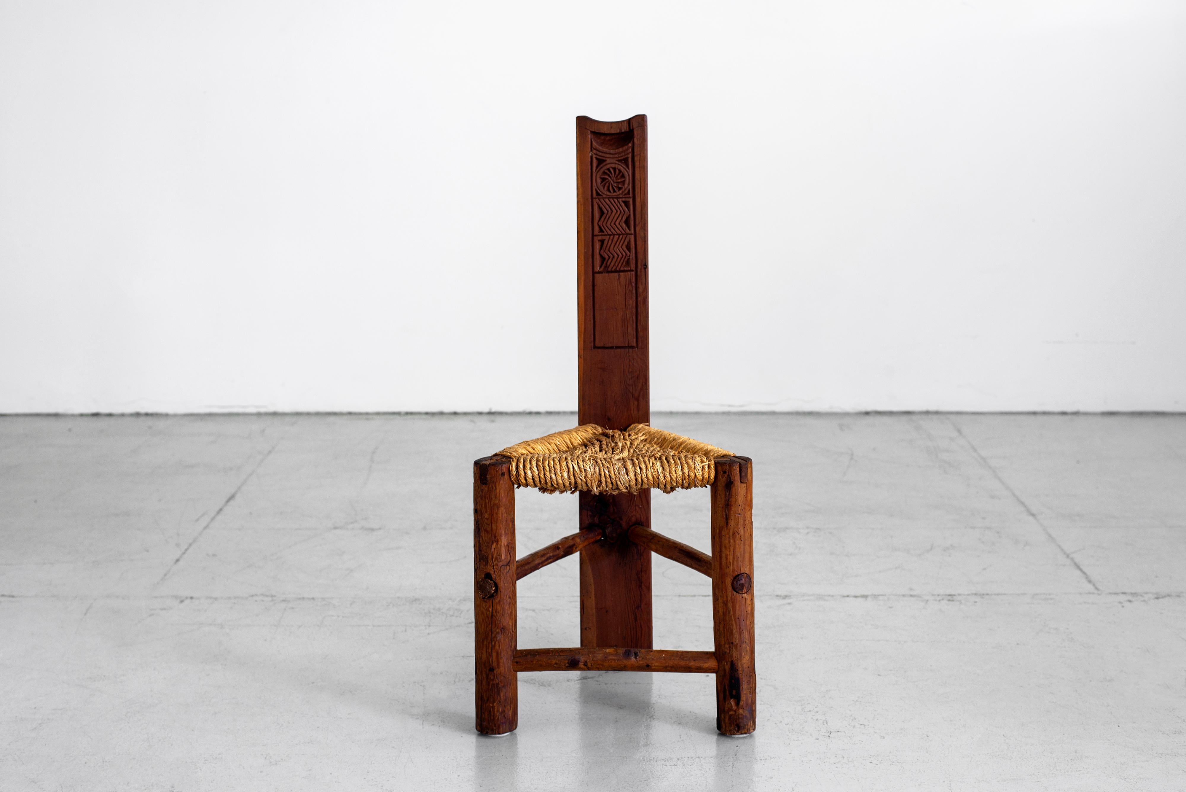 Primitive triangular wood chair with detailed carving and woven rush seat.