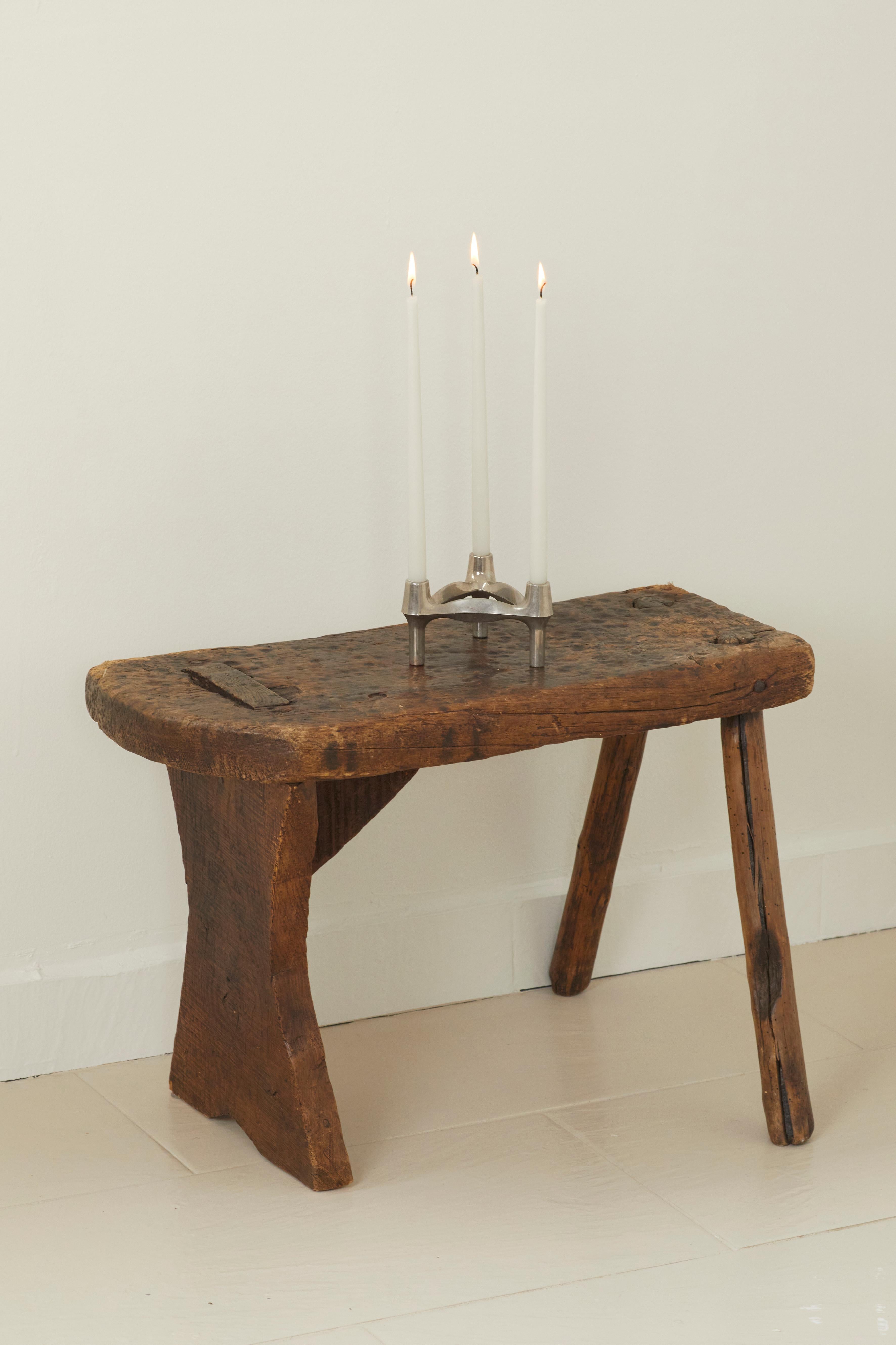 A beautifully aged primitive, rustic stool made from an even older bench, France, c. 1900. Carved and shaped by hand in solid wood. Will support the weight of decorative objects but not sturdy enough to sit on.