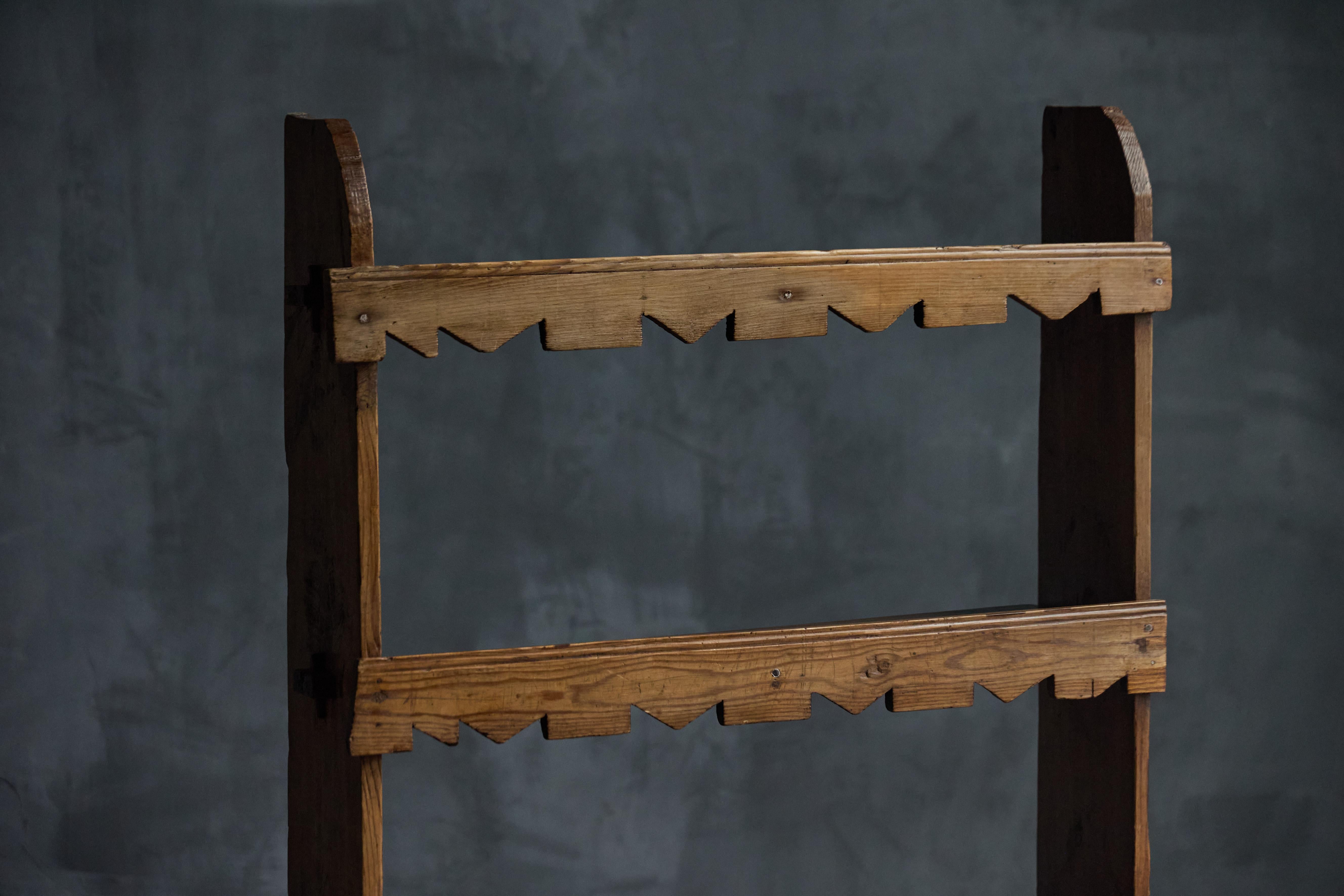 Una graziosa libreria in legno caratterizzata da un motivo giocoso lungo i suoi ripiani, che aggiunge un tocco di estrosità al suo design rustico. Il telaio robusto e la struttura aperta lo rendono un pezzo versatile, perfetto per esporre libri,