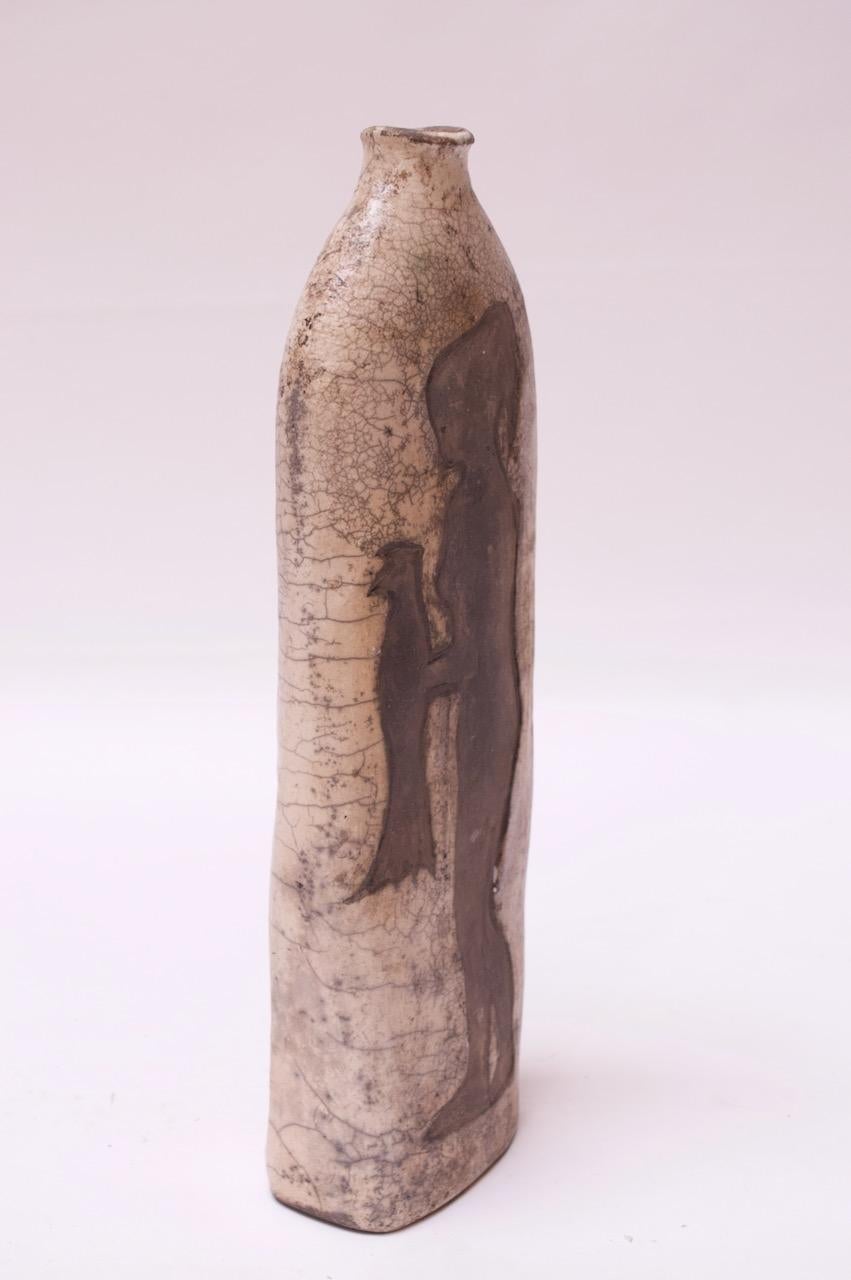 Primitive studio ceramic vase with woman with bird motif present on both sides (figure differs only slightly from side to side). 
Crazing both from age and by design. Although, designed in 1972, the piece is intended to look much older. 
Couple of