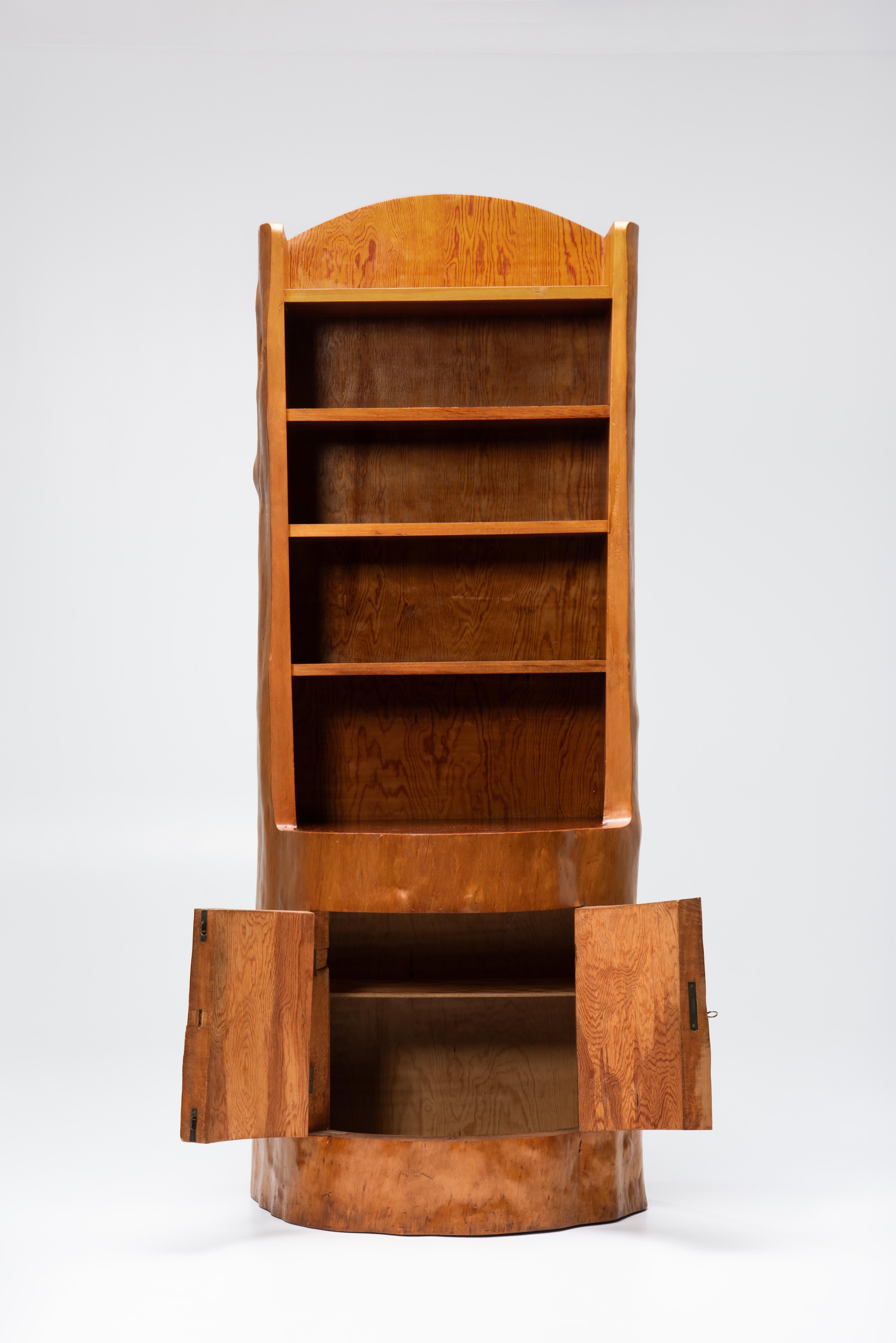 This distinctive cabinet, crafted from a single pine tree trunk, represents a unique example of traditional folk art. The bar cabinet features two doors at the base, carved from the trunk, and four shelves at the summit. The exterior has been