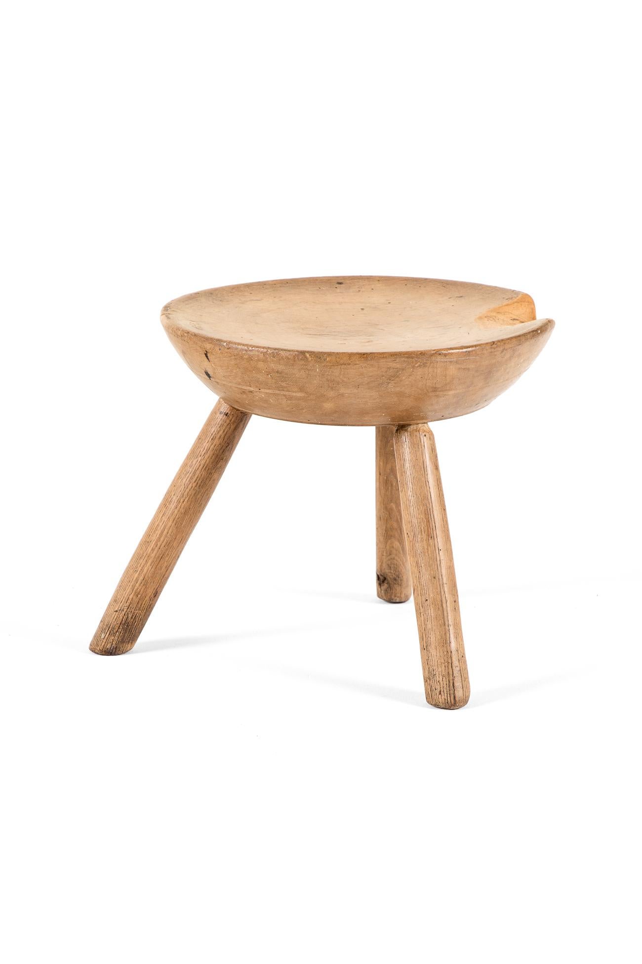 A low 19th century primitive elm milking stool raised on three stout legs.

The stool would have been crafted using a hand operated lathe to achieve the rounded smooth surface to the thick top.

The top displays a section missing, smoothed over time