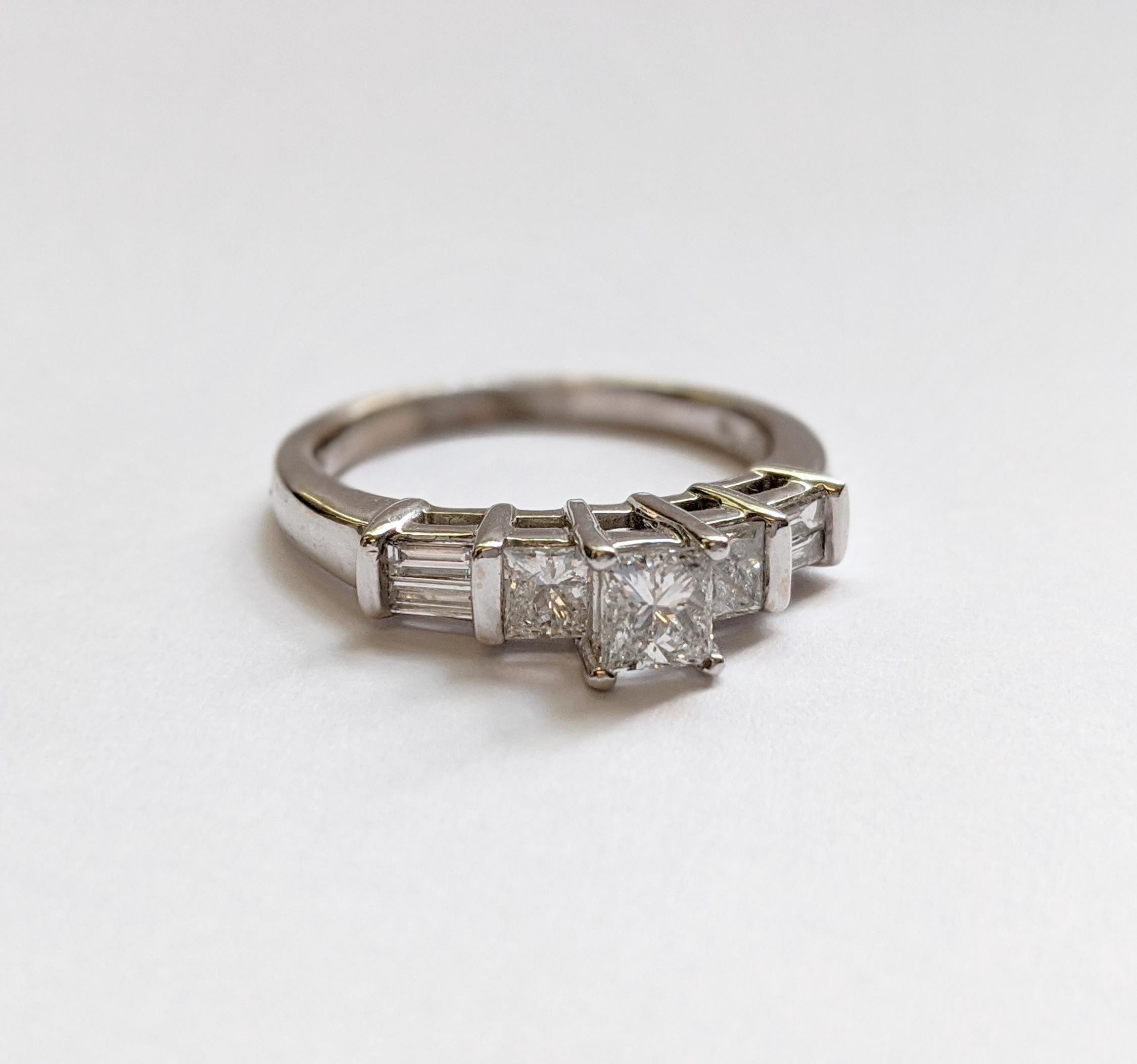 This ring will make any modern-day princess gleam. This contemporary engagement ring features a princess-cut diamond in the center.  Two princess cut and four baguette diamonds on either side frame the center stone. Fashioned in polished 14K white