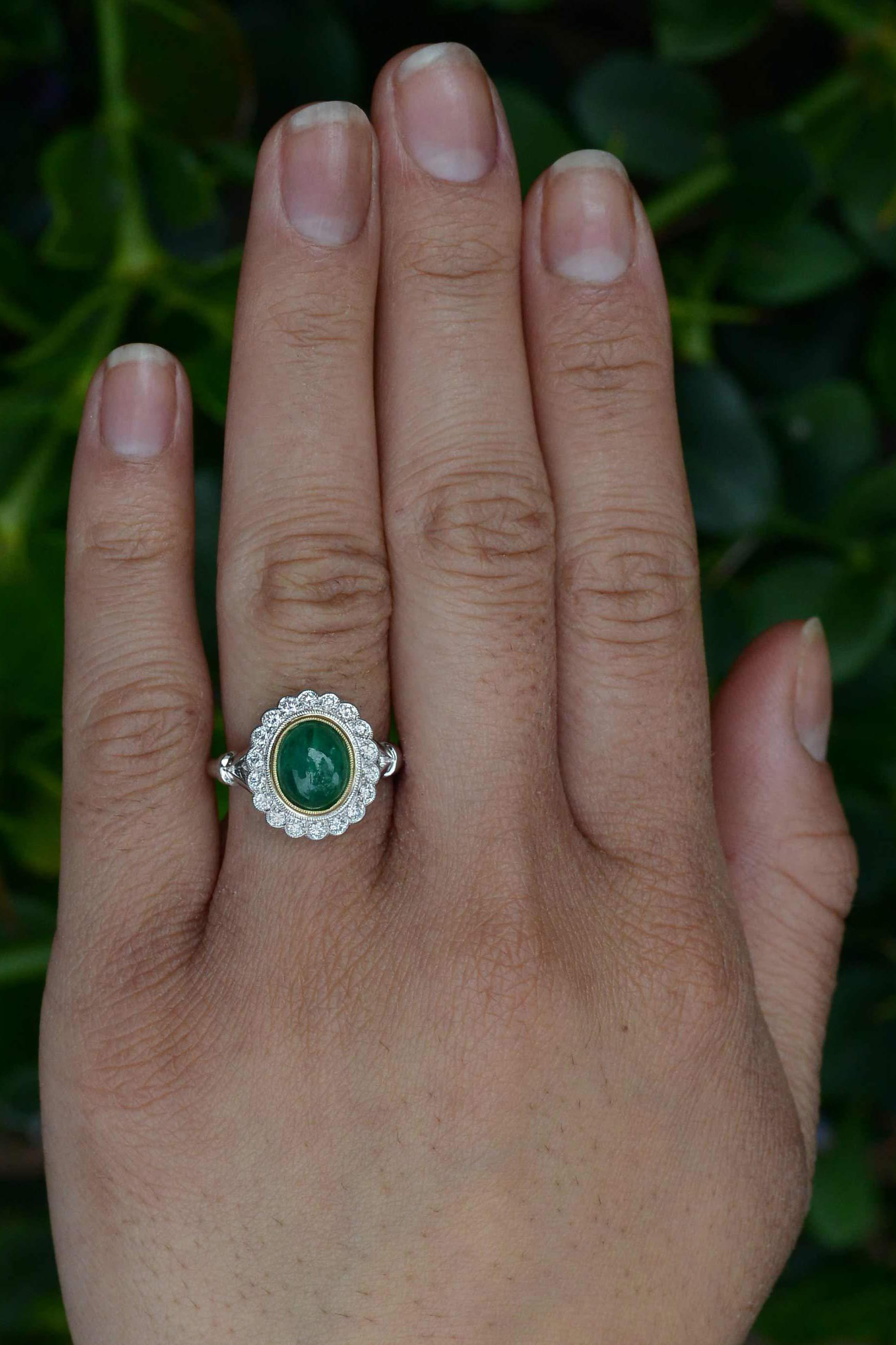 A classic emerald engagement ring. Centered by a glowing oval cabochon near 2 carat emerald with a lush, vibrant, medium-dark green, complimented by a yellow gold bezel. The scalloped and milgrained 1/2 Ct. diamond halo adds a sparkling, fiery