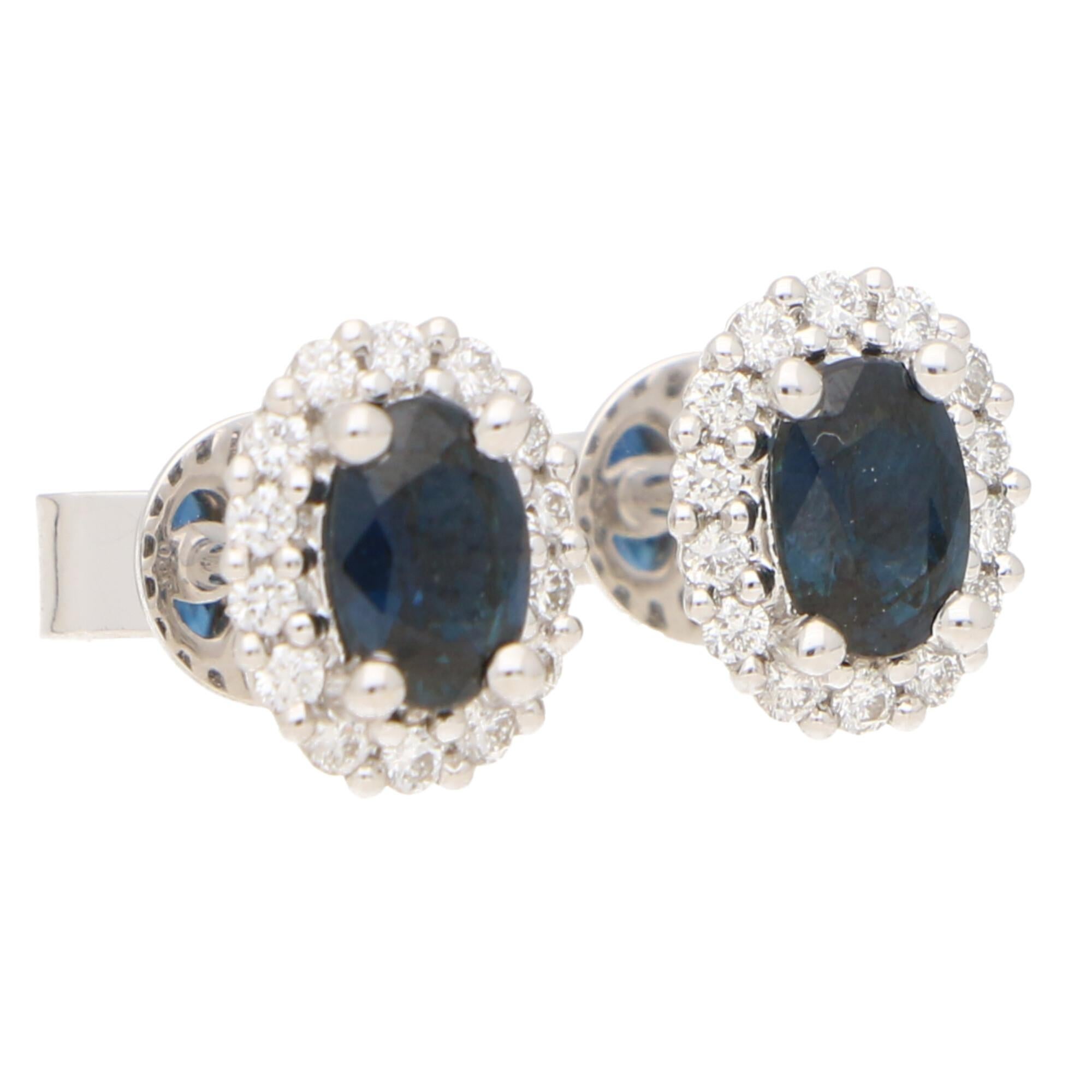A lovely pair of sapphire and diamond oval halo earrings set in 18k white gold.

Each earring centrally features a beautiful deep blue coloured oval shaped sapphire surrounded by a halo of 16 round brilliant-cut diamonds. All of the stones are set