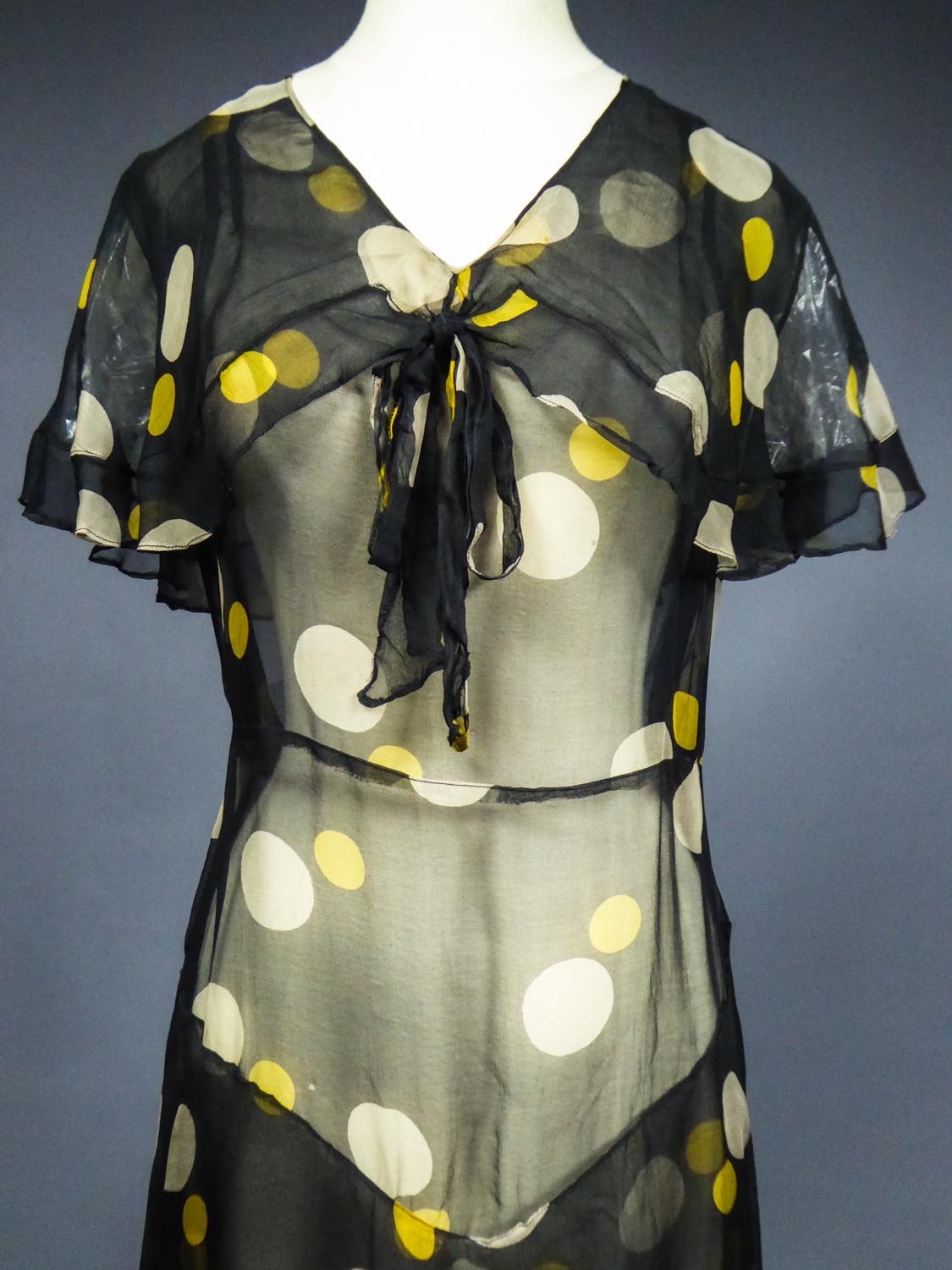 Circa 1930/1935
France

Summer dress in black muslin printed chiffon with large yellow and white polka dots from the 1930s. Straight and fluid dress with integrated shawl covering the shoulders and closing with a matching bow. Skirt with two large