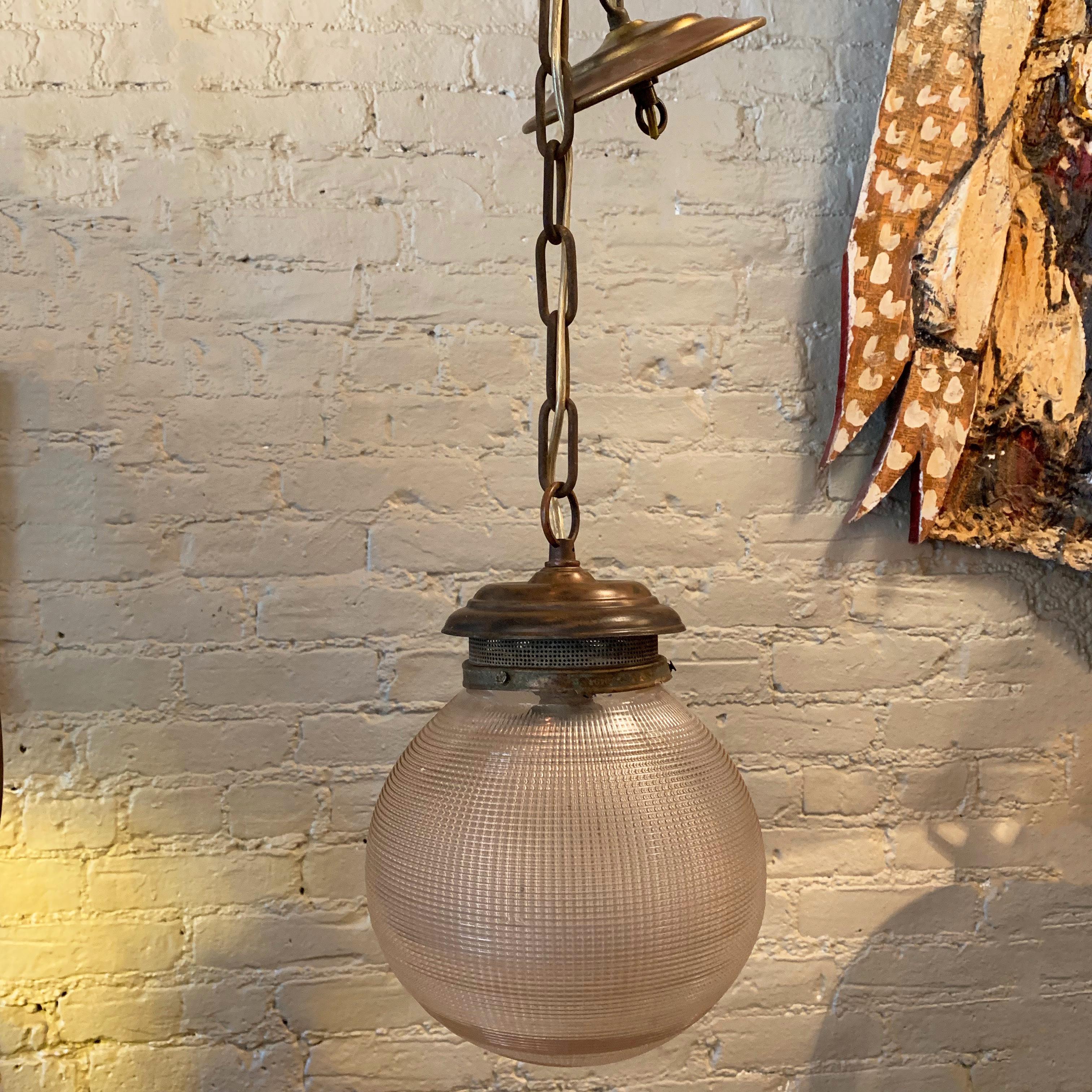 Early 20th century, industrial pendant light features an 8 inch, prismatic, Holophane glass globe shade with a brass fitter, chain and ceiling canopy. The full hanging length if the pendant is 37 inches.