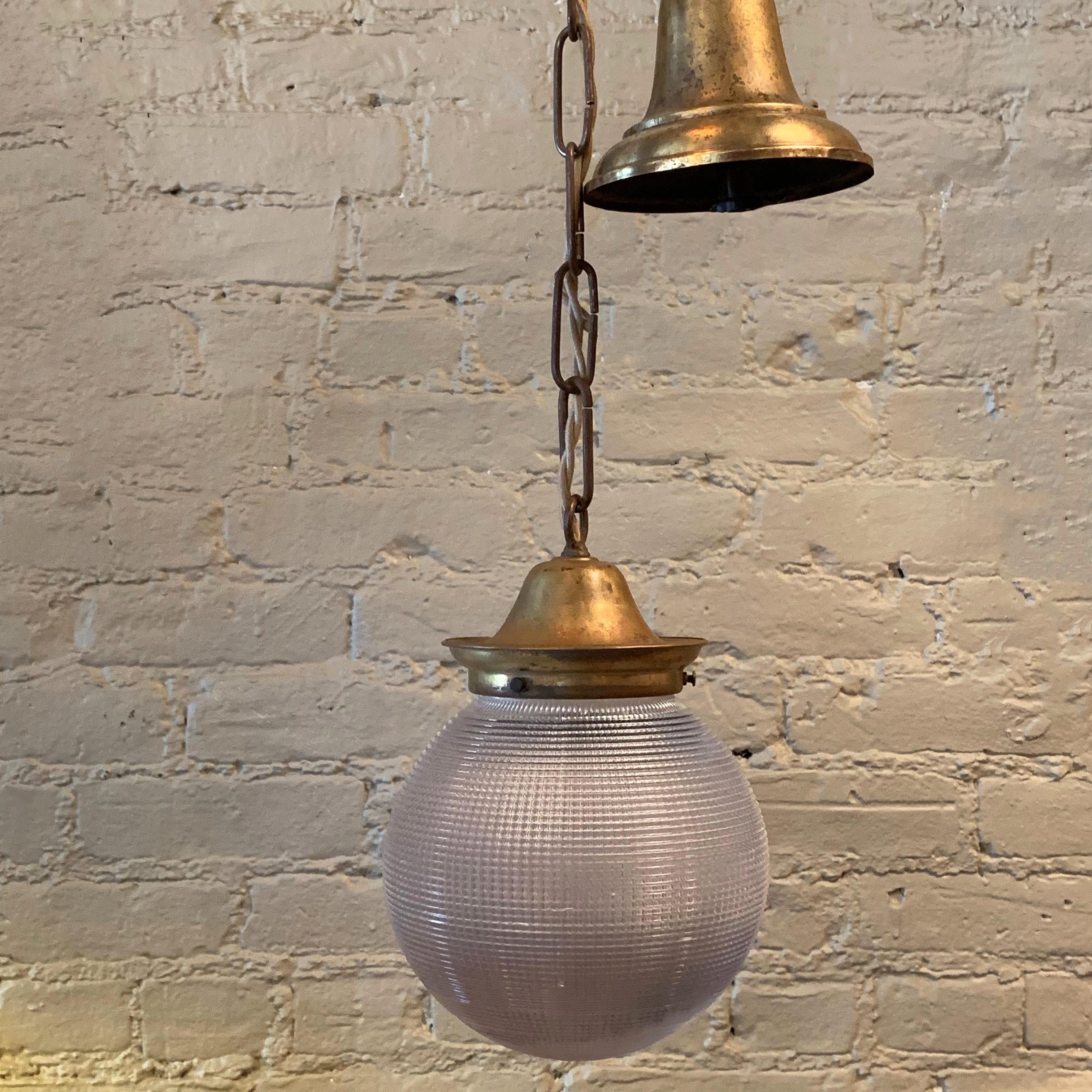 Early 20th century, industrial pendant light features a prismatic Holophane glass globe shade with a brass fitter, chain and ceiling canopy. The full hanging length if the pendant is 37 inches.