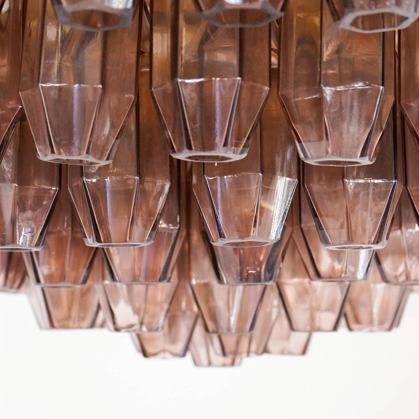 A splendid cluster of 169 mouth-blown amber glass elements shaped like pencils imbues this chandelier with a luxurious charm. Thanks to a special double magnifying lens design, each glass element contributes to the clever concealing of the brass