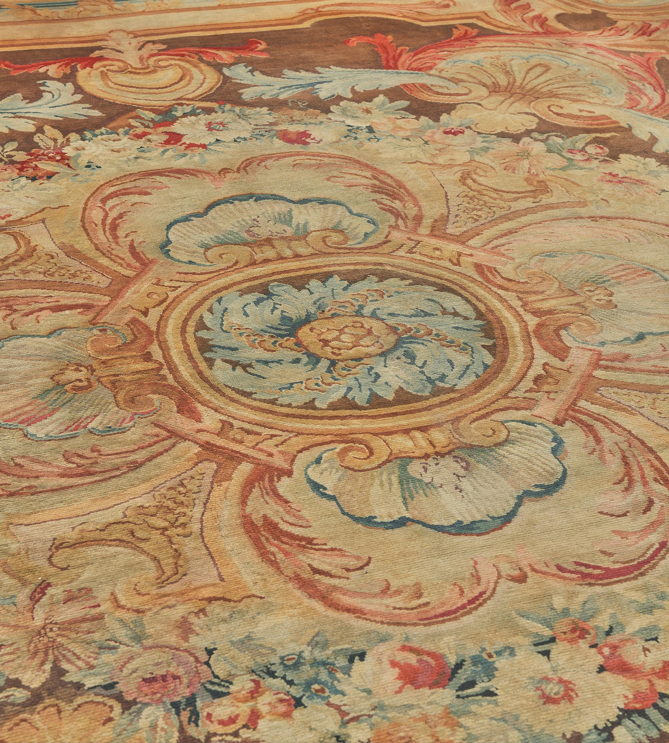 This antique, circa 1860, French Savonnerie rug has a soft chocolate-brown field with an outer sandy-yellow frame panel issuing inward brick-red acanthus leaves containing a shell motif and paired light blue acanthus leaves around a large central
