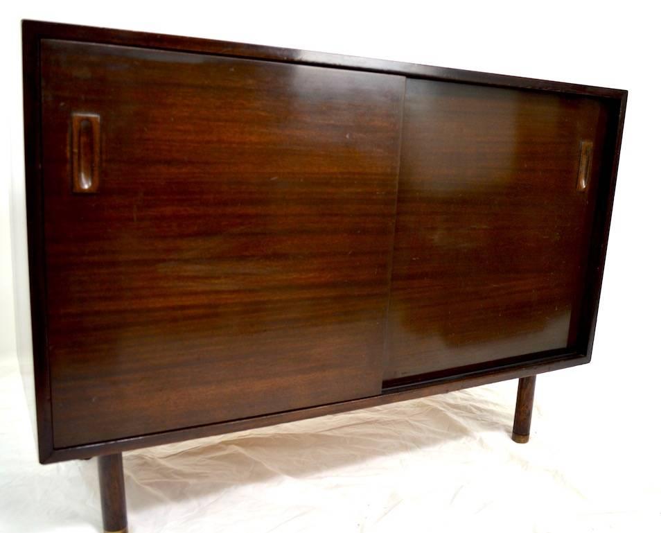 Dark mahogany two sliding door cabinet. One side opens to interior drawers, the other opens to an adjustable shelf. Good, original, unrestored condition, showing some cosmetic wear to finish, normal and consistent with age. The back legs are missing