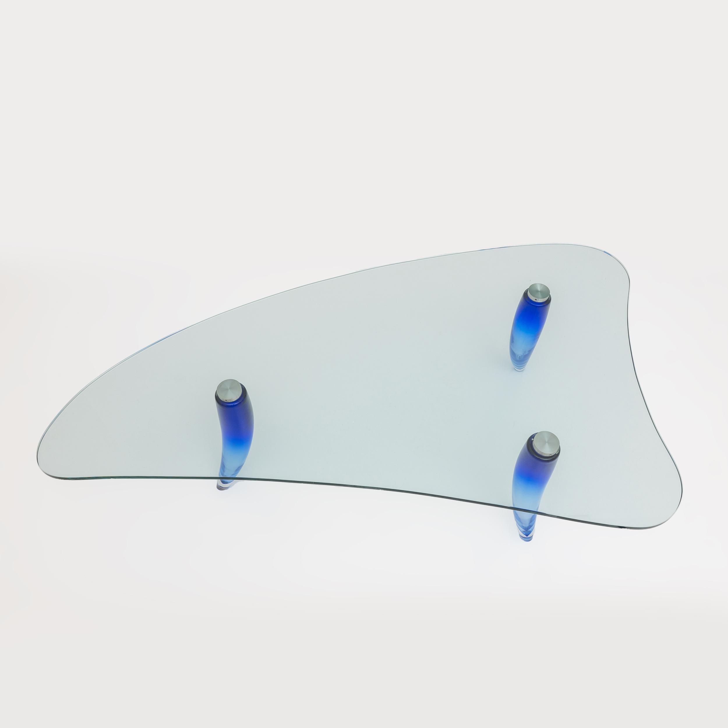 Coffee table, designed by Maurice Barilone for Roche Bobois and produced by the Murano glassworks Seguso. Three-legged structure with a transparent glass top in a triangular shape with rounded corners and edges, conical feet in blue and transparent