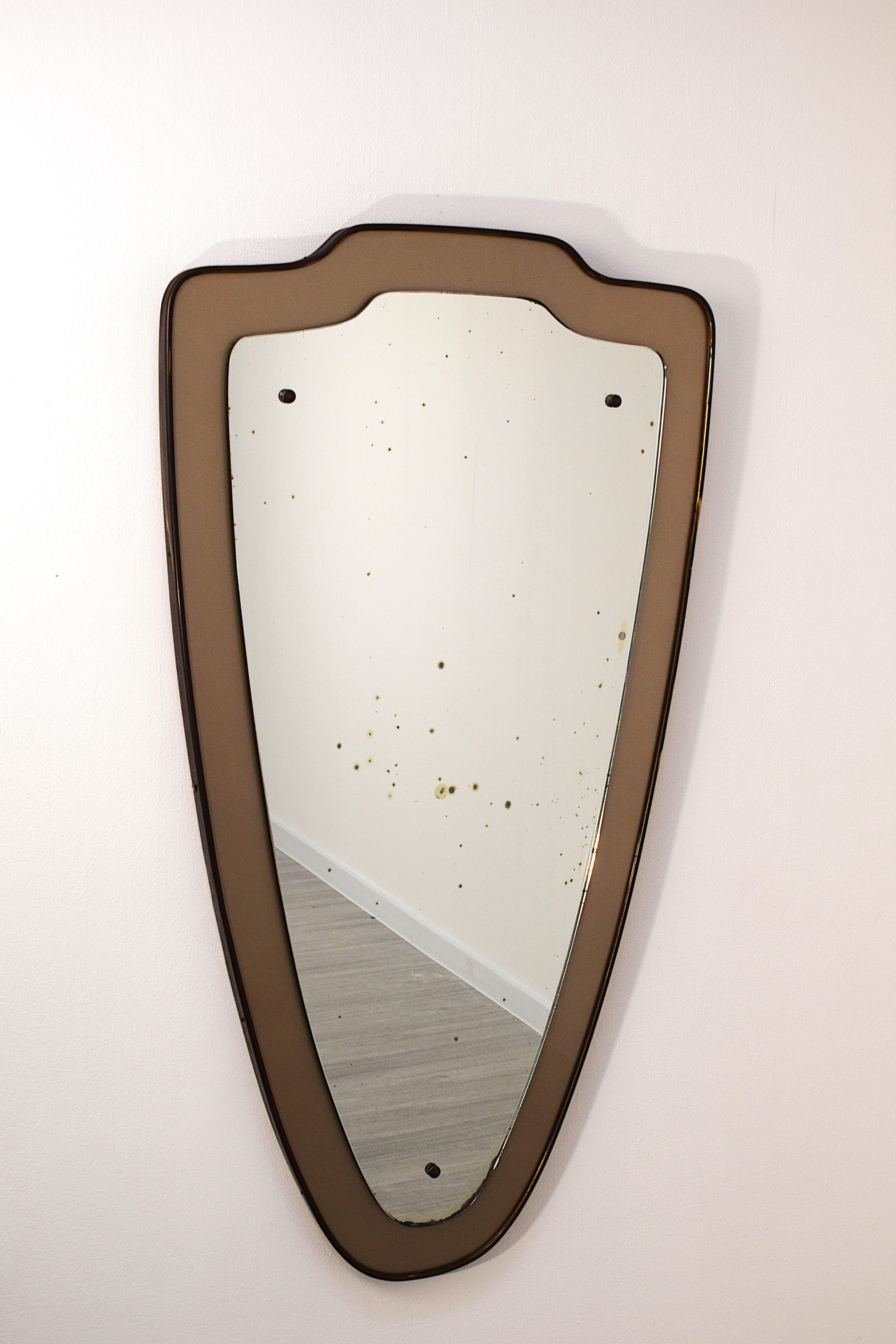Miroir italien des années 1950 avec un élégant cadre en laiton et cristal coloré, un exemple authentique du design vintage du milieu du siècle. La structure, en bois, présente une forme harmonieuse et raffinée, enrichie par des détails en laiton qui