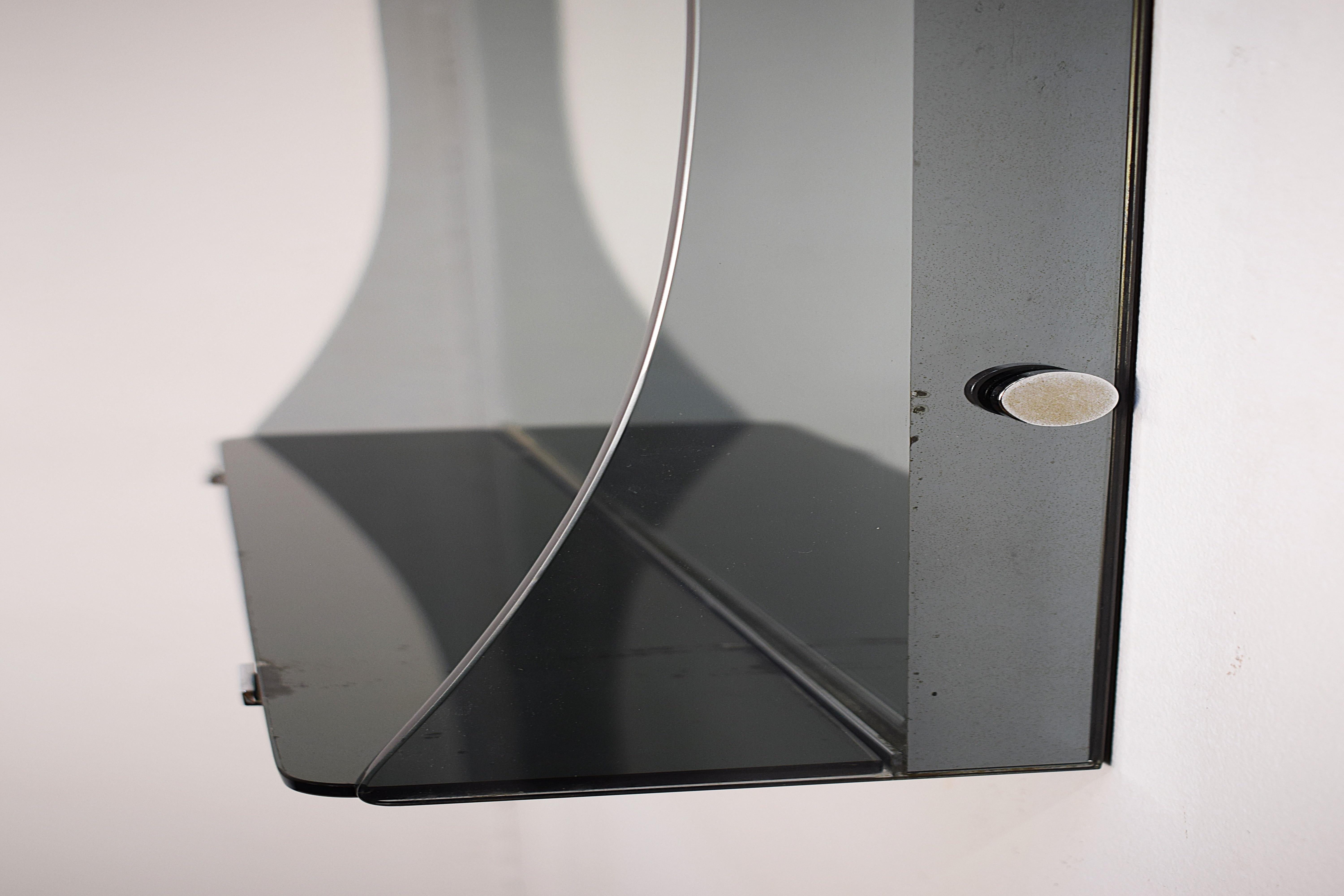 Specchiera italiana in vetro fumé, anni ’70, dal design elegante e minimalista. Realizzata con materiali di qualità – vetro, vetro specchiato e metallo – questa specchiera si distingue per la sua forma essenziale e la pratica mensola integrata,