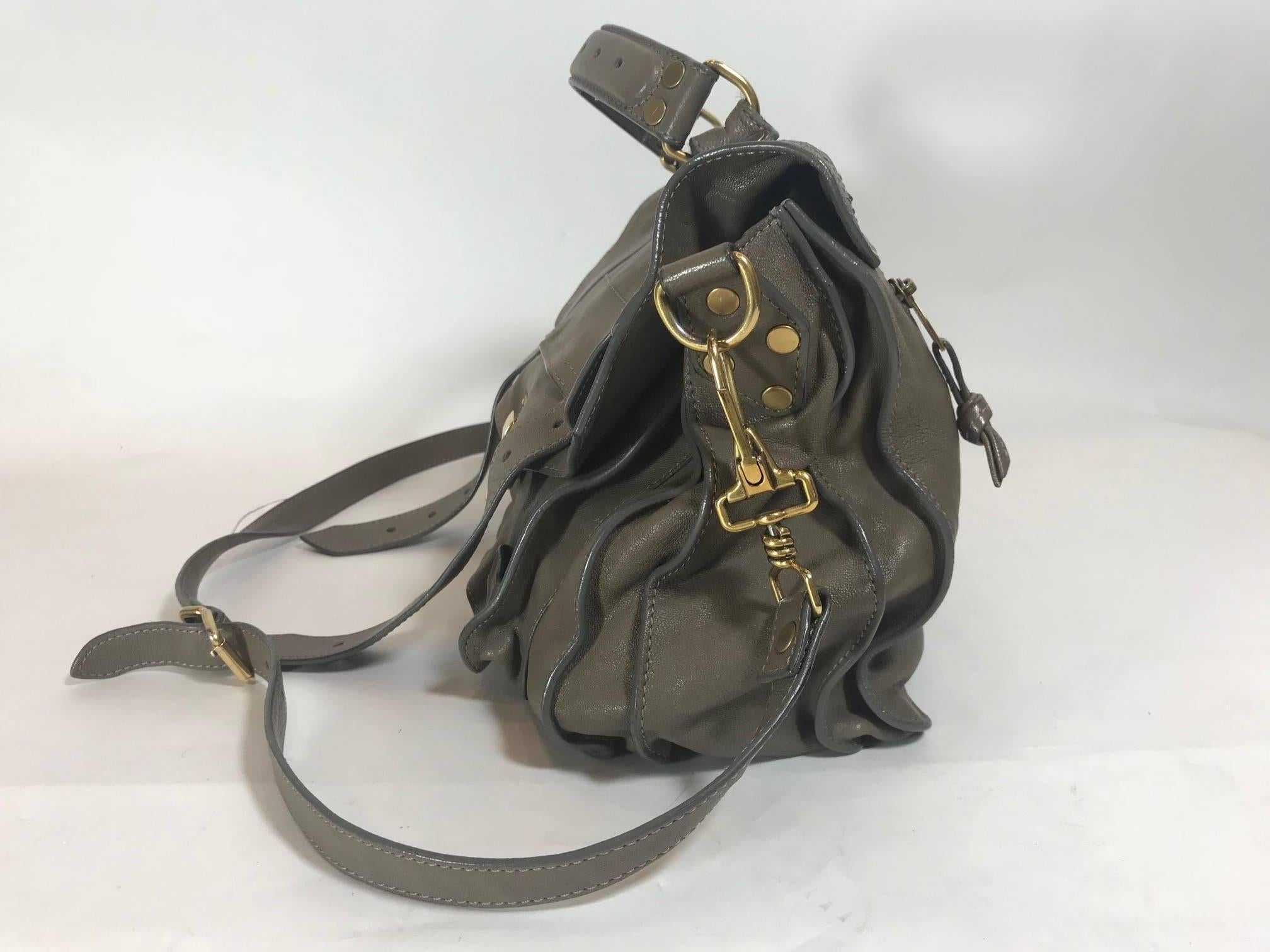 Taupe leather. Gold-tone hardware. Flip-lock featuring dual pull-through closures at front flap. Detachable flat shoulder strap. Single flat top handle. Exterior zip pocket at back. Dual pockets at flap underside. Grey jacquard woven lining. Single