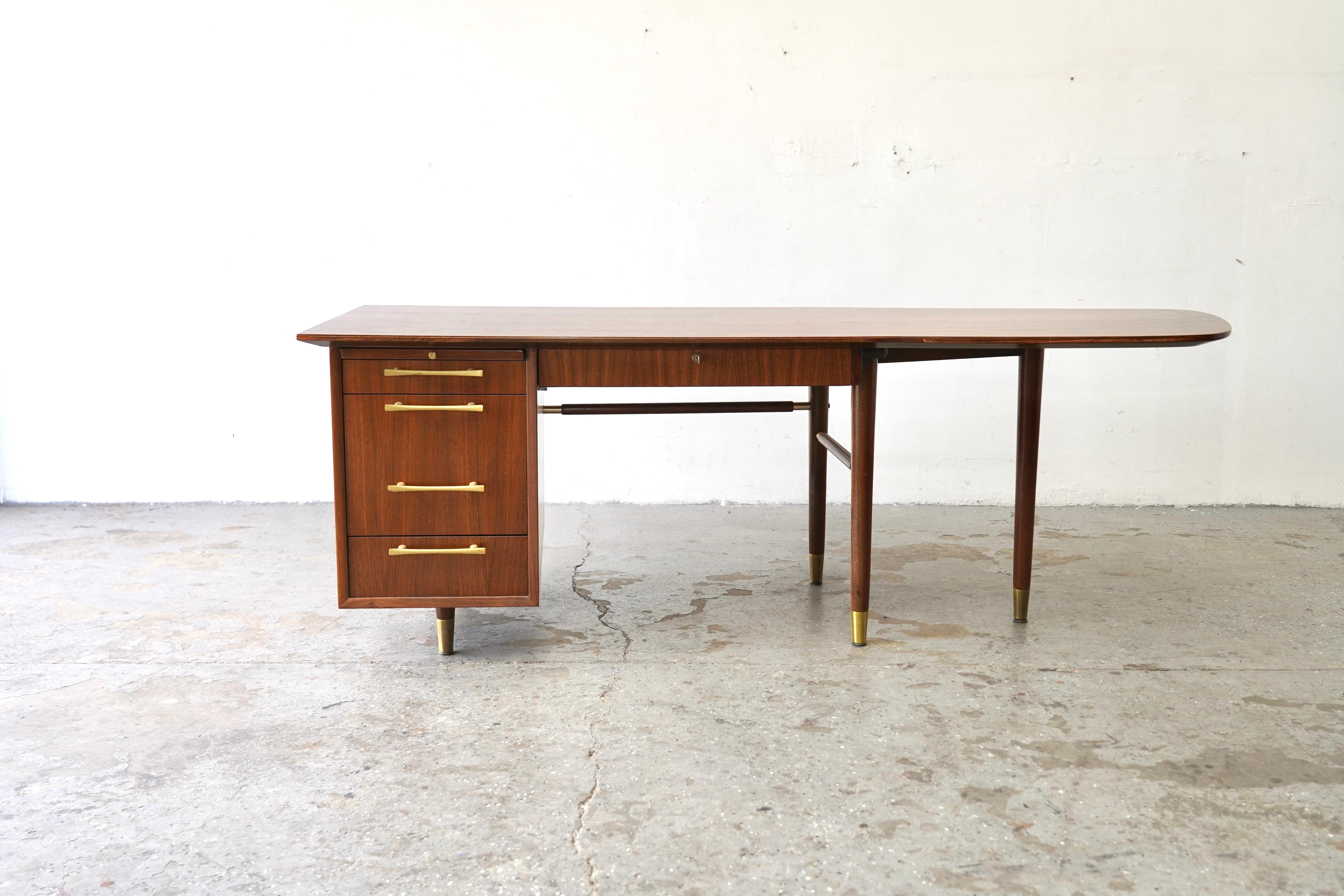 This is a beautifully restored  Mid-Century Modern  walnut executive desk featuring a unique boomerang-shaped top with stunning walnut grain. A shared mechanism locks all four drawers when the bolt on the center desk drawer is locked. Stamped